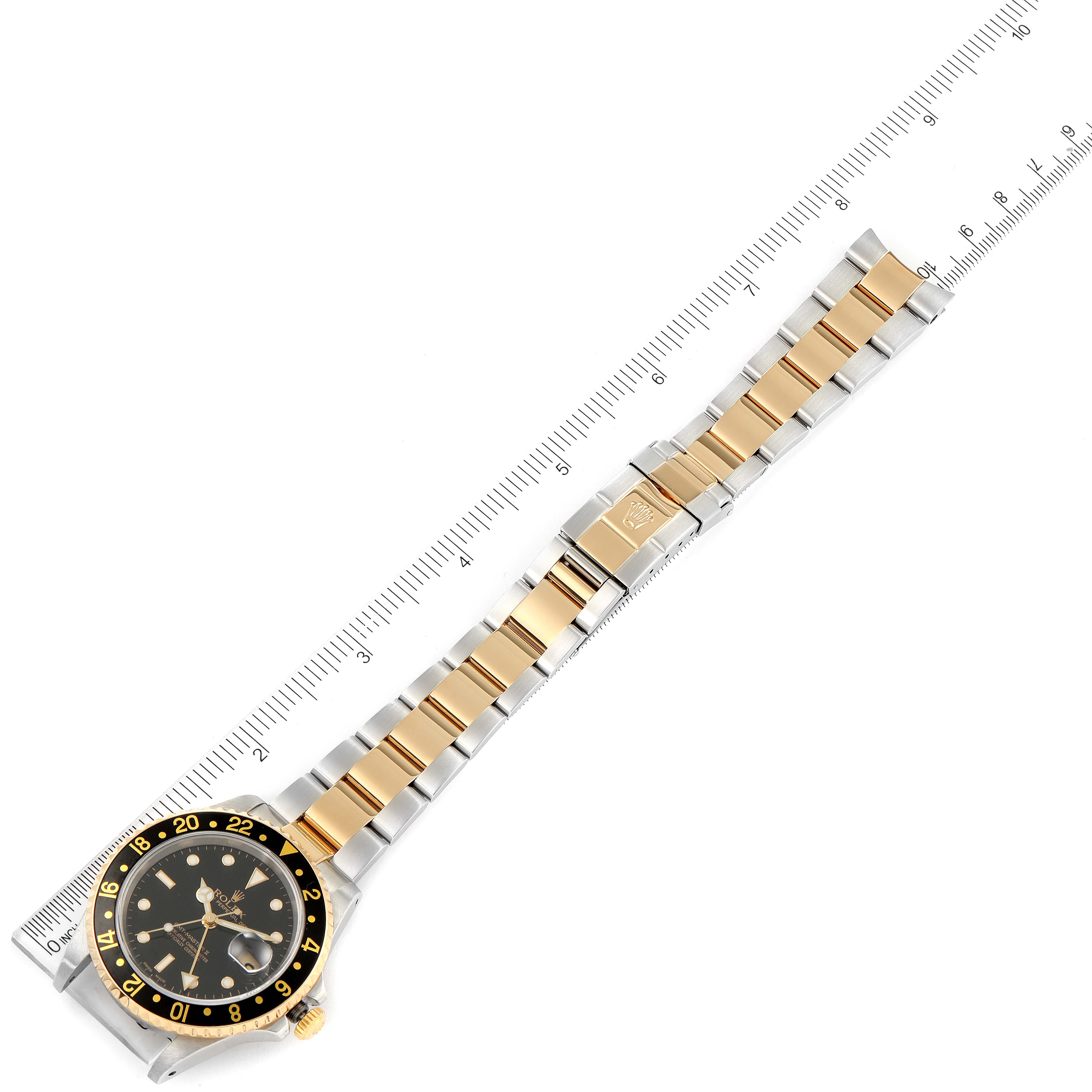 The image shows a top-down view of a Rolex GMT-Master 16713 Men's Steel and Gold (two tone) Black Dial 16713 Men's Steel and Gold (two tone) Black Dial watch, including the bezel, dial, and full two-tone bracelet with a ruler for scale.