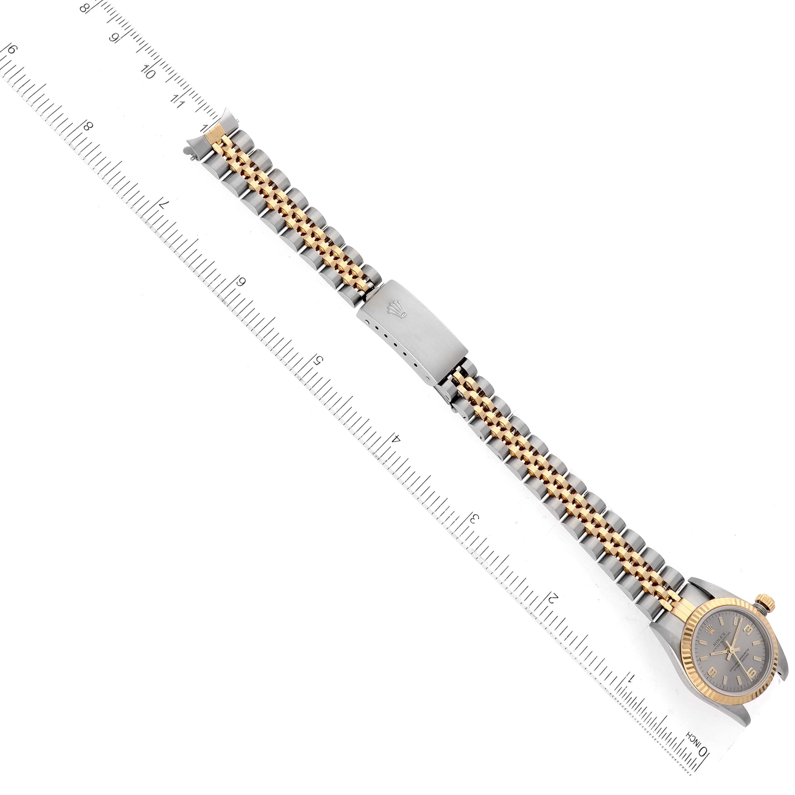 The image shows the front view of a Rolex Oyster Perpetual 76193 Women's Steel and Gold (two tone) Silver Dial 76193 Women's Steel and Gold (two tone) Silver Dial watch laid flat with an attached ruler for scale measurement.
