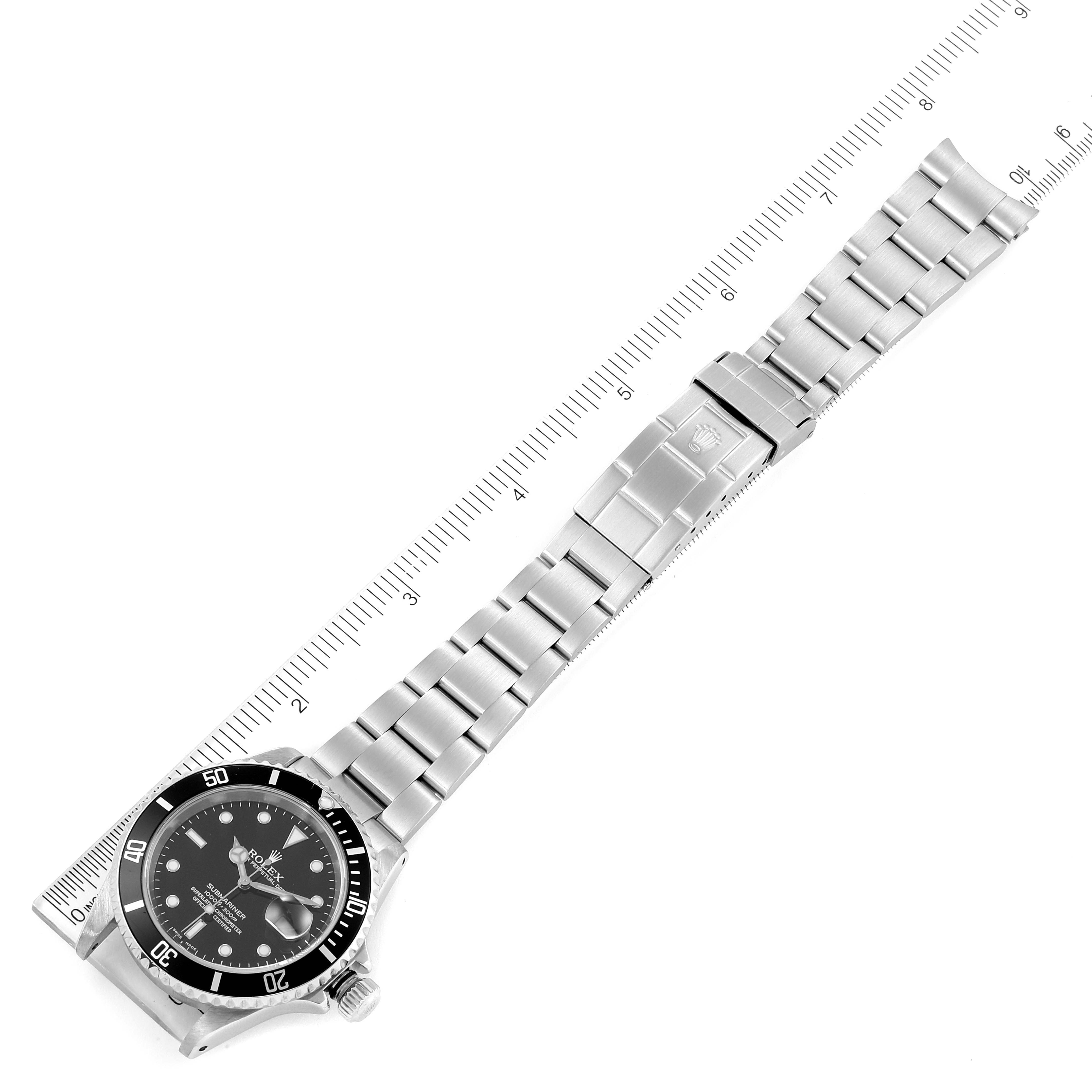 The image shows a full view of the Rolex Submariner 16610 Men's Stainless Steel Black Dial 16610 Men's Stainless Steel Black Dial watch from an overhead angle, including its dial, bezel, band, and clasp, alongside a ruler for scale.