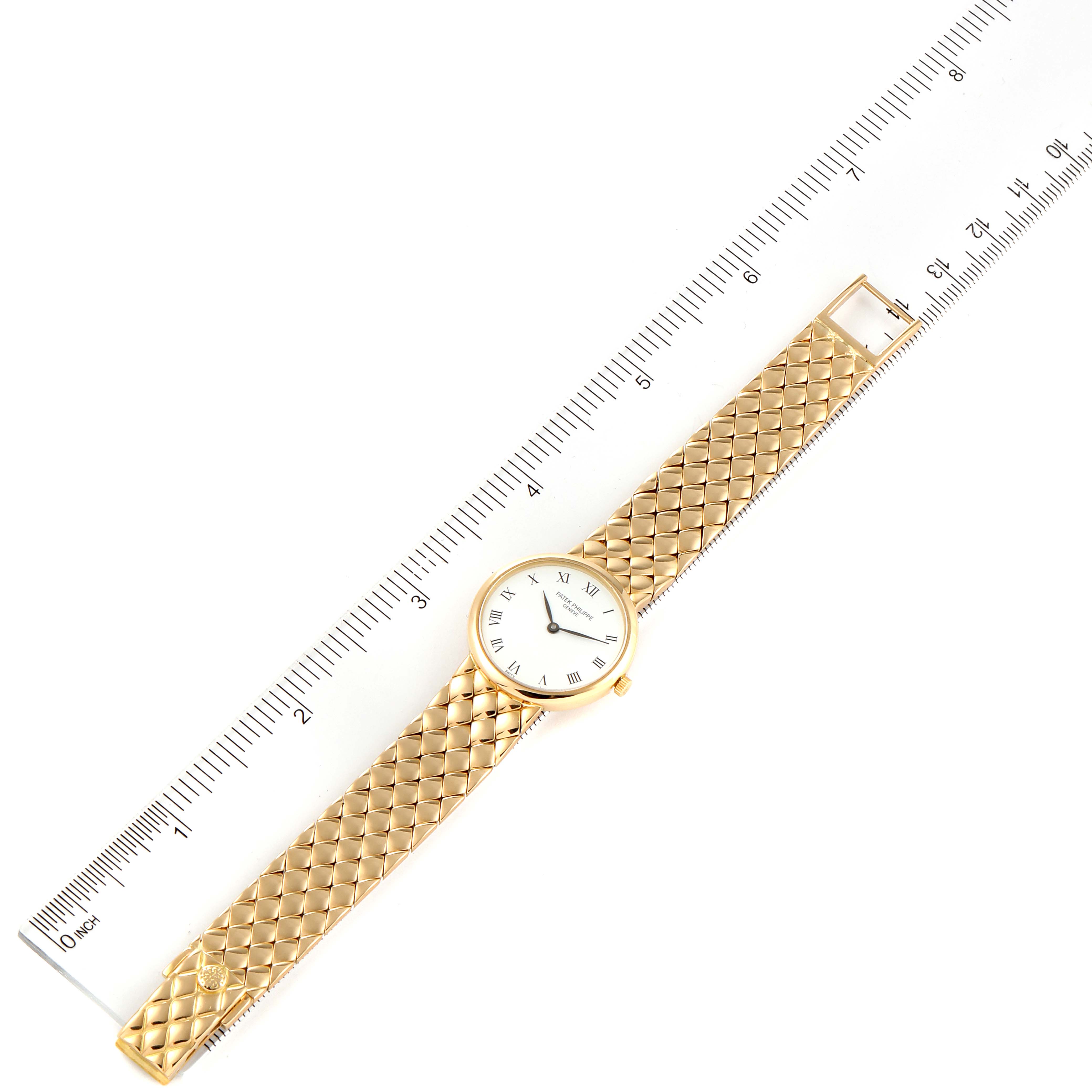 The image shows a top-down view of a Patek Philippe Calatrava 4821 Women's Yellow Gold White Dial 4821 Women's Yellow Gold White Dial watch, including the face, case, and woven gold bracelet placed alongside a ruler.