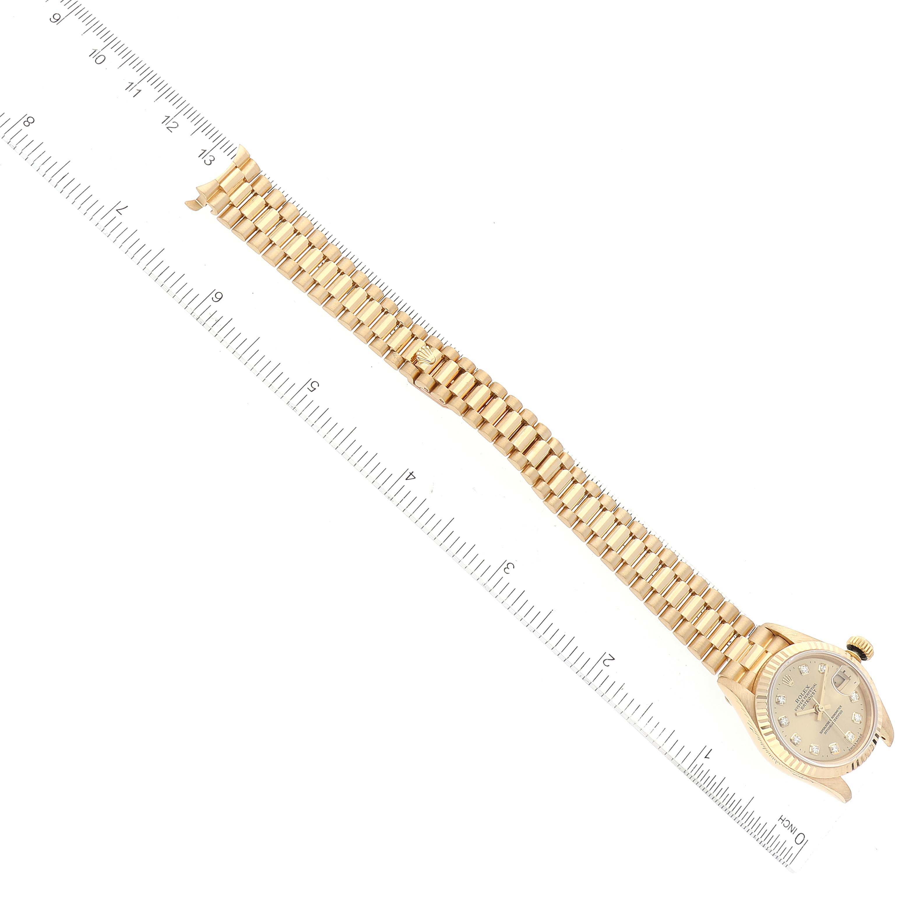 The image shows a Rolex President 69178 Women
s Yellow Gold Champagne Dial 69178 Women
s Yellow Gold Champagne Dial model watch from an overhead angle, featuring the face and full bracelet next to a ruler for scale.