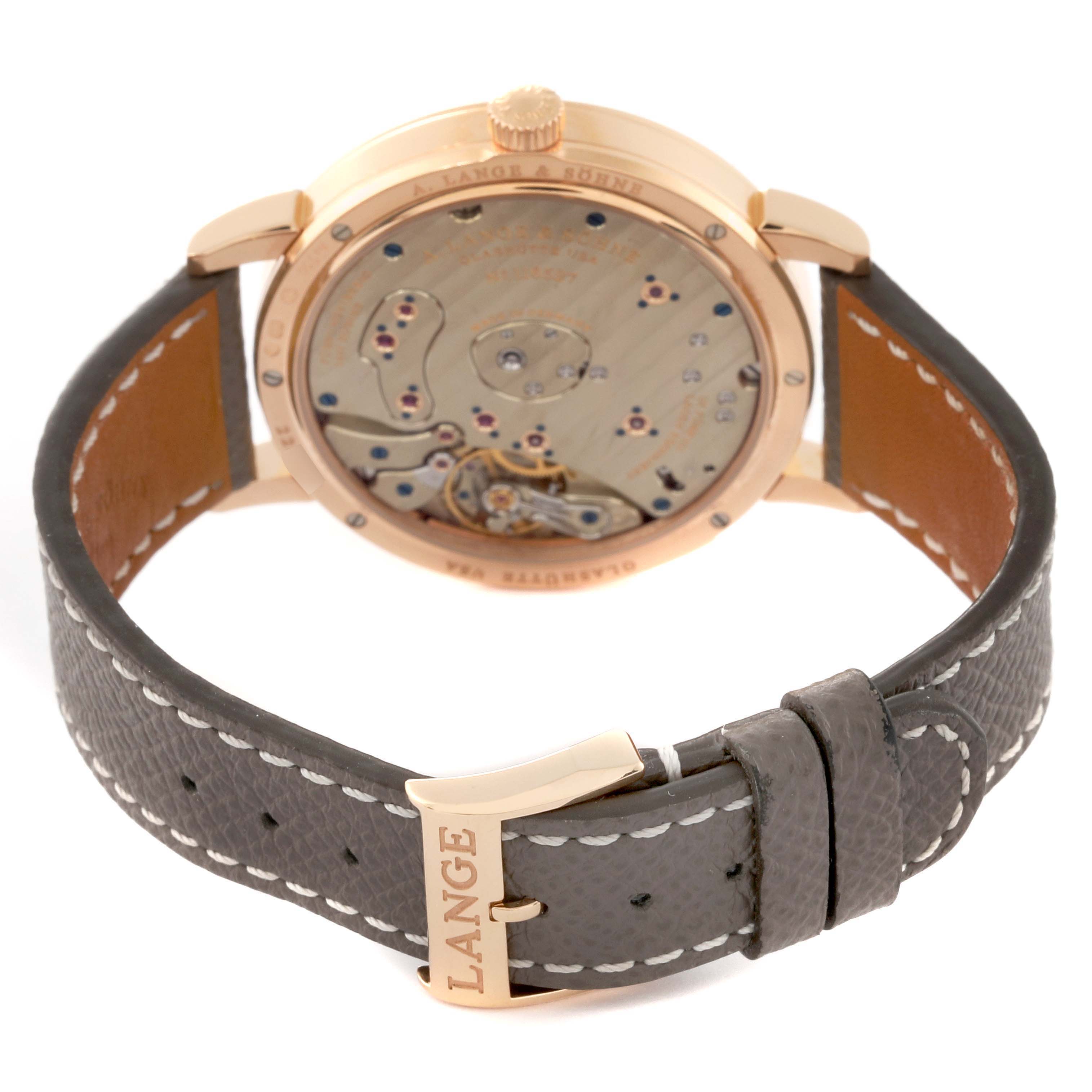 The image shows the back of the A. Lange & Sohne Lange 1 139.032 Men's Rose Gold Silver Dial watch, highlighting its movement and leather strap with a buckle.