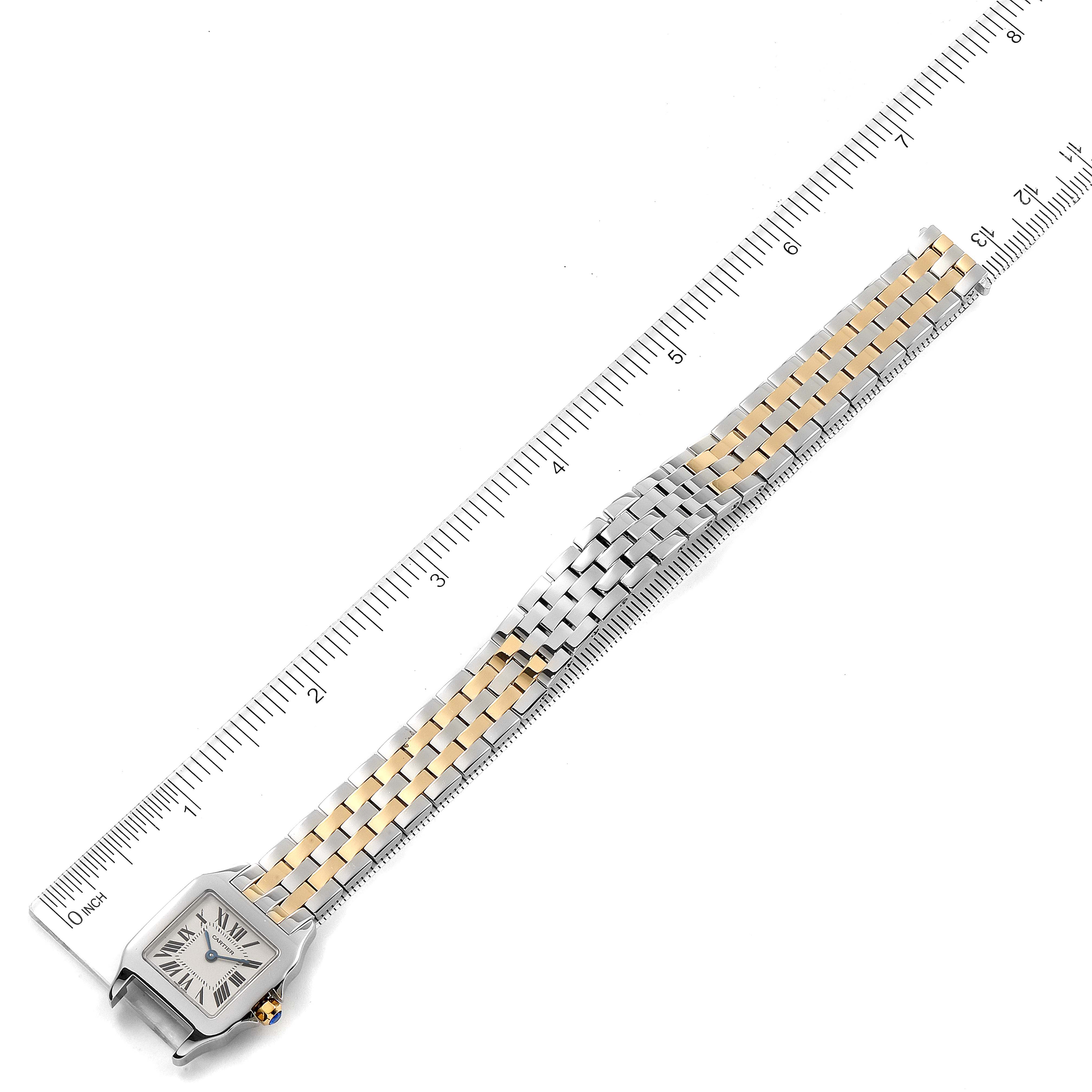 The image shows a Cartier Santos Demoiselle W25066Z6 Women
s Steel and Gold (two tone) Silver Dial W25066Z6 Women
s Steel and Gold (two tone) Silver Dial watch laid flat, highlighting its face, and two-tone metal bracelet, alongside a ruler for scale.