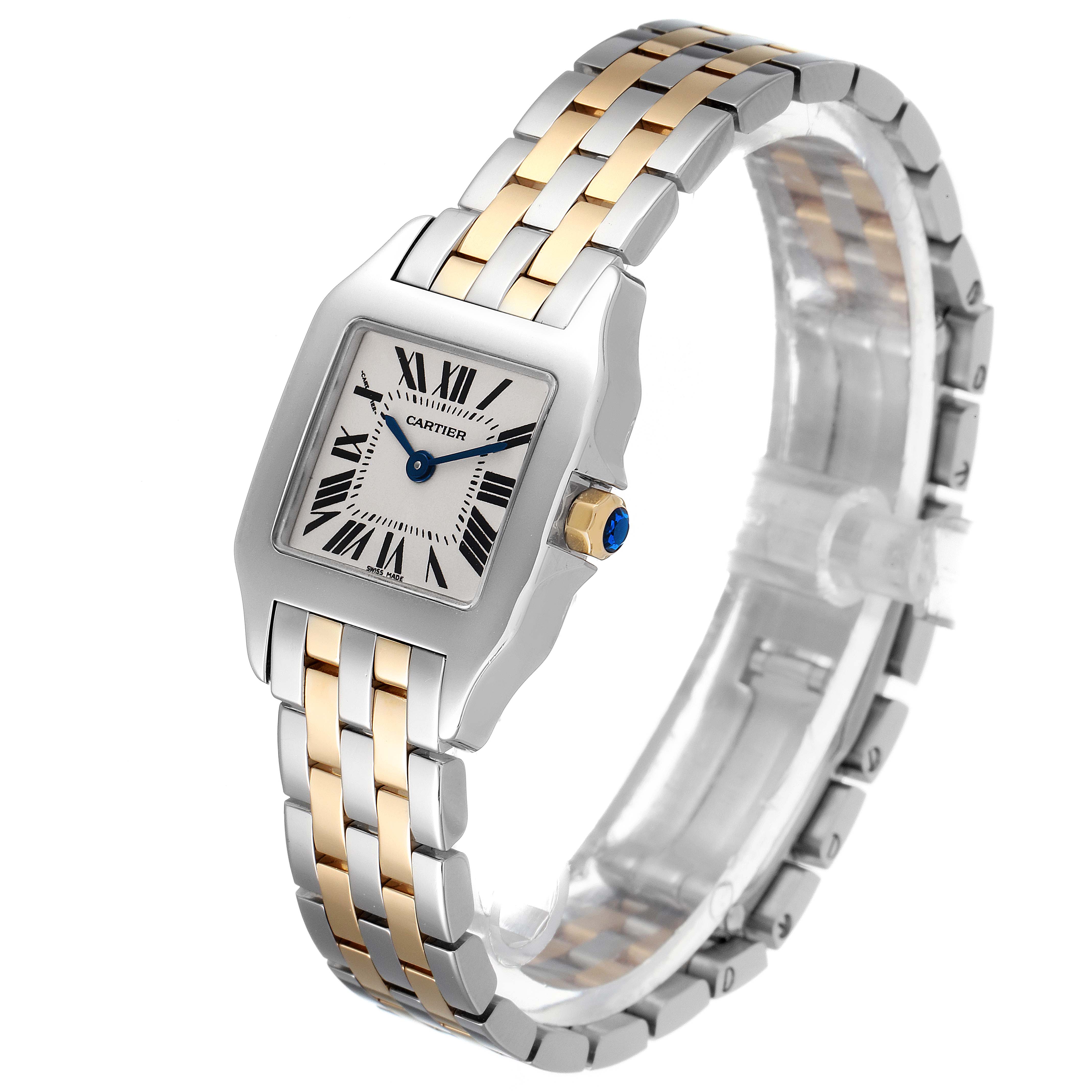 The image shows a Cartier Santos Demoiselle W25066Z6 Women
s Steel and Gold (two tone) Silver Dial W25066Z6 Women
s Steel and Gold (two tone) Silver Dial watch at a three-quarter angle, highlighting its face, two-tone bracelet, and the crown with a blue gem.