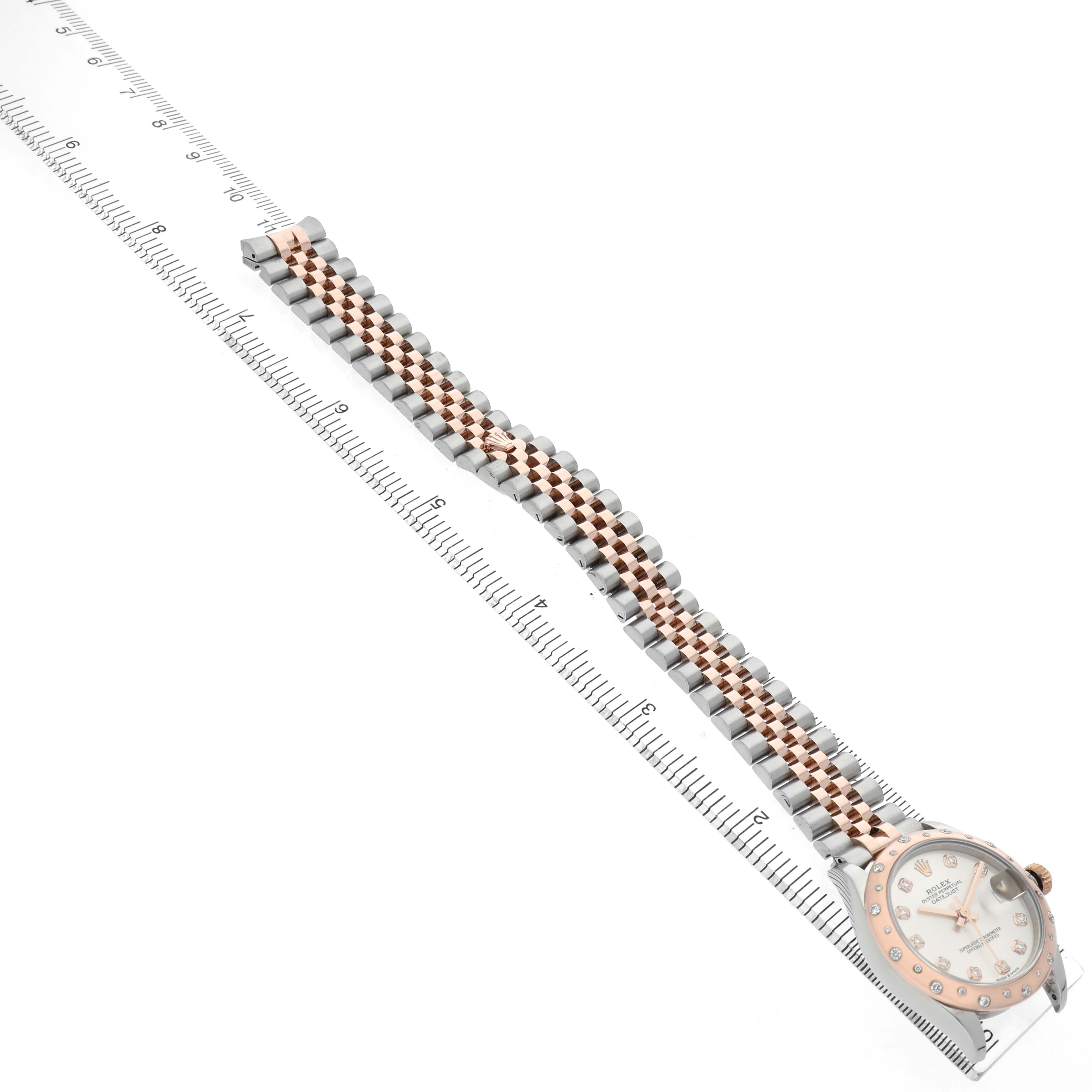 The Rolex Mid-Size M278341RBR-0016 Women's Steel and Gold (two tone) Silver Dial watch is shown from a top-down angle, featuring the face, bezel, and two-tone bracelet alongside a ruler.