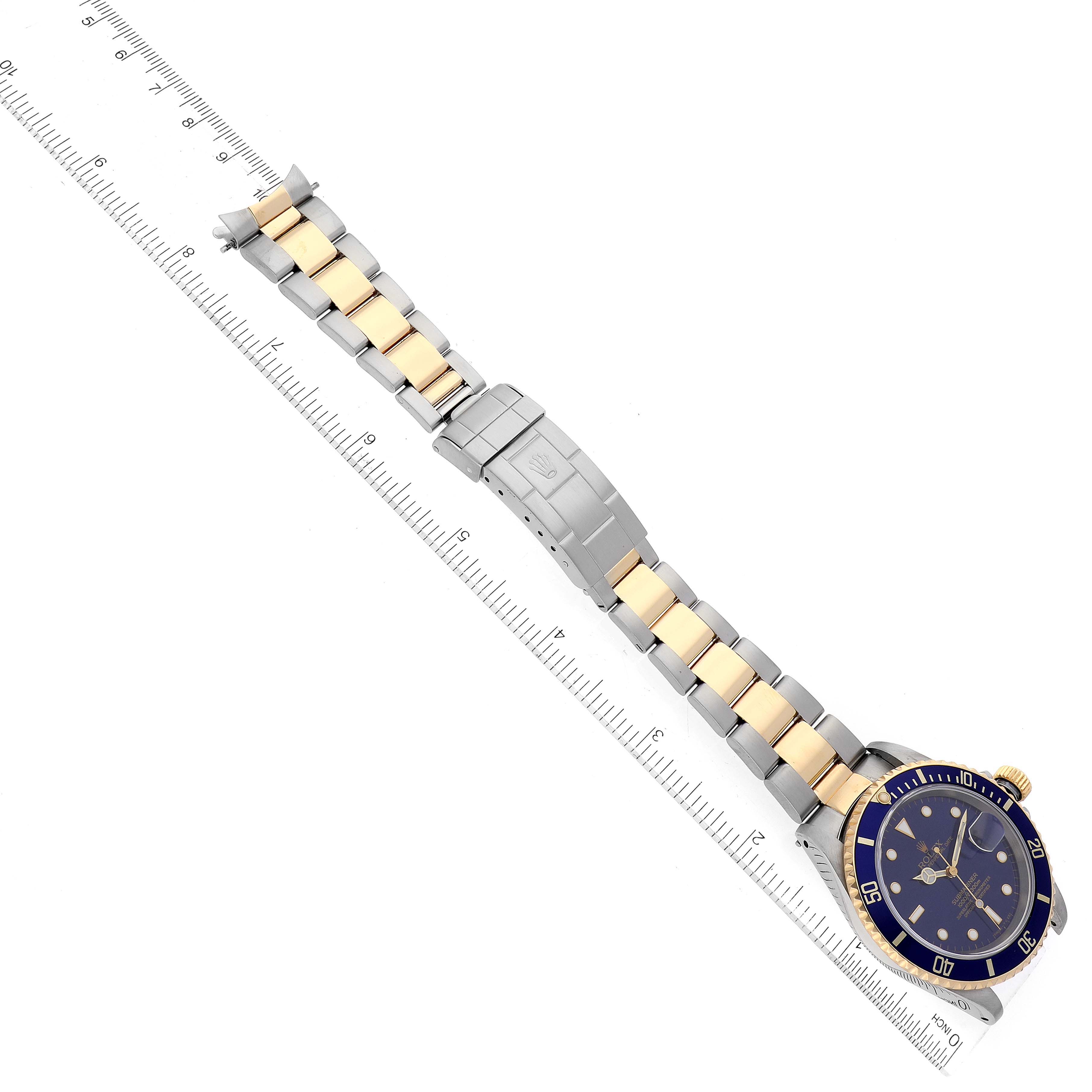 The Rolex Submariner 16613 Men's Steel and Gold (two tone) Blue Dial 16613 Men's Steel and Gold (two tone) Blue Dial watch is shown from a top-down angle, displaying the entire band and face laid flat next to a ruler.