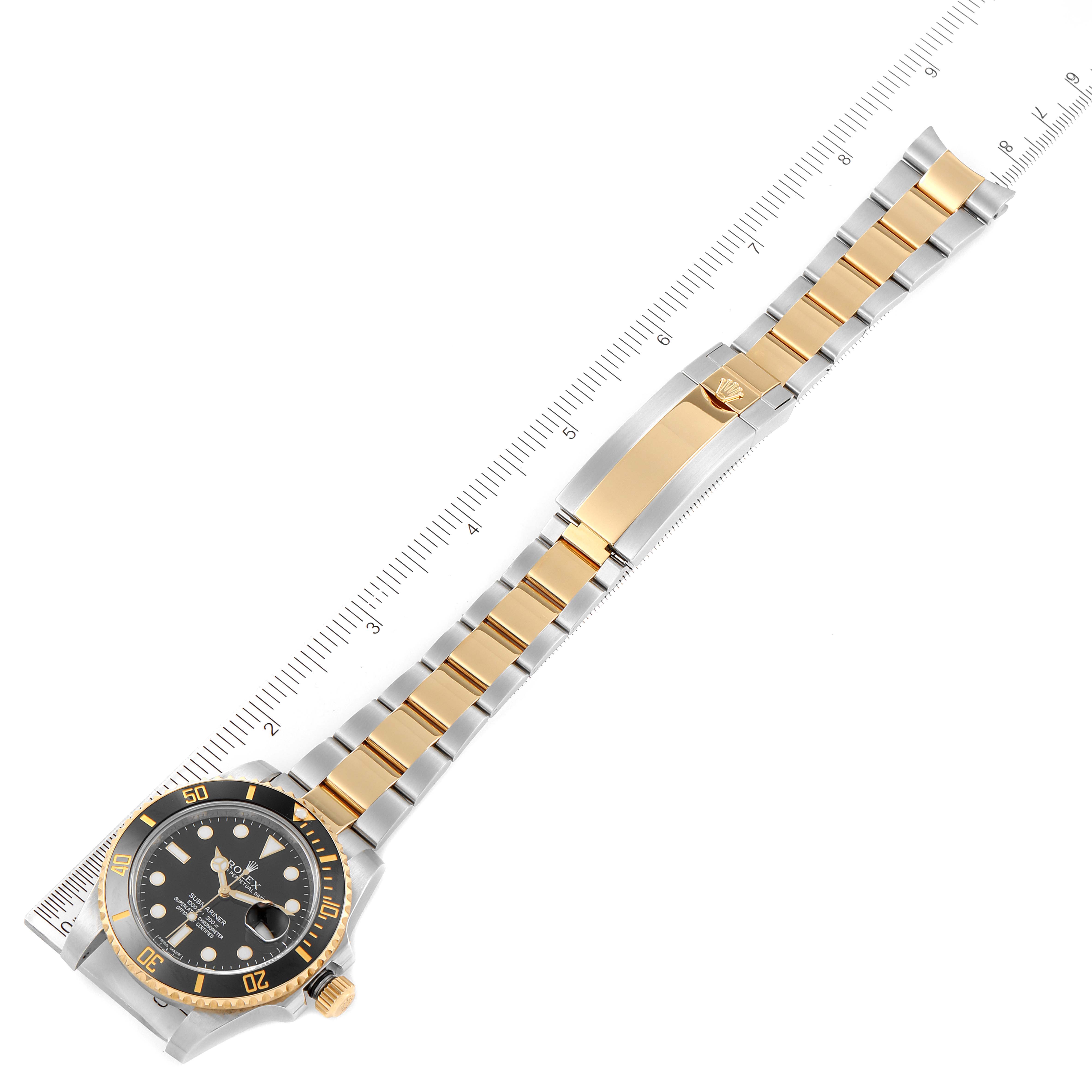 The image shows a top view of a Rolex Submariner 116613 Men's Steel and Gold (two tone) Black Dial 116613 Men's Steel and Gold (two tone) Black Dial watch, displaying its dial, bezel, and two-tone bracelet with a ruler for scale.