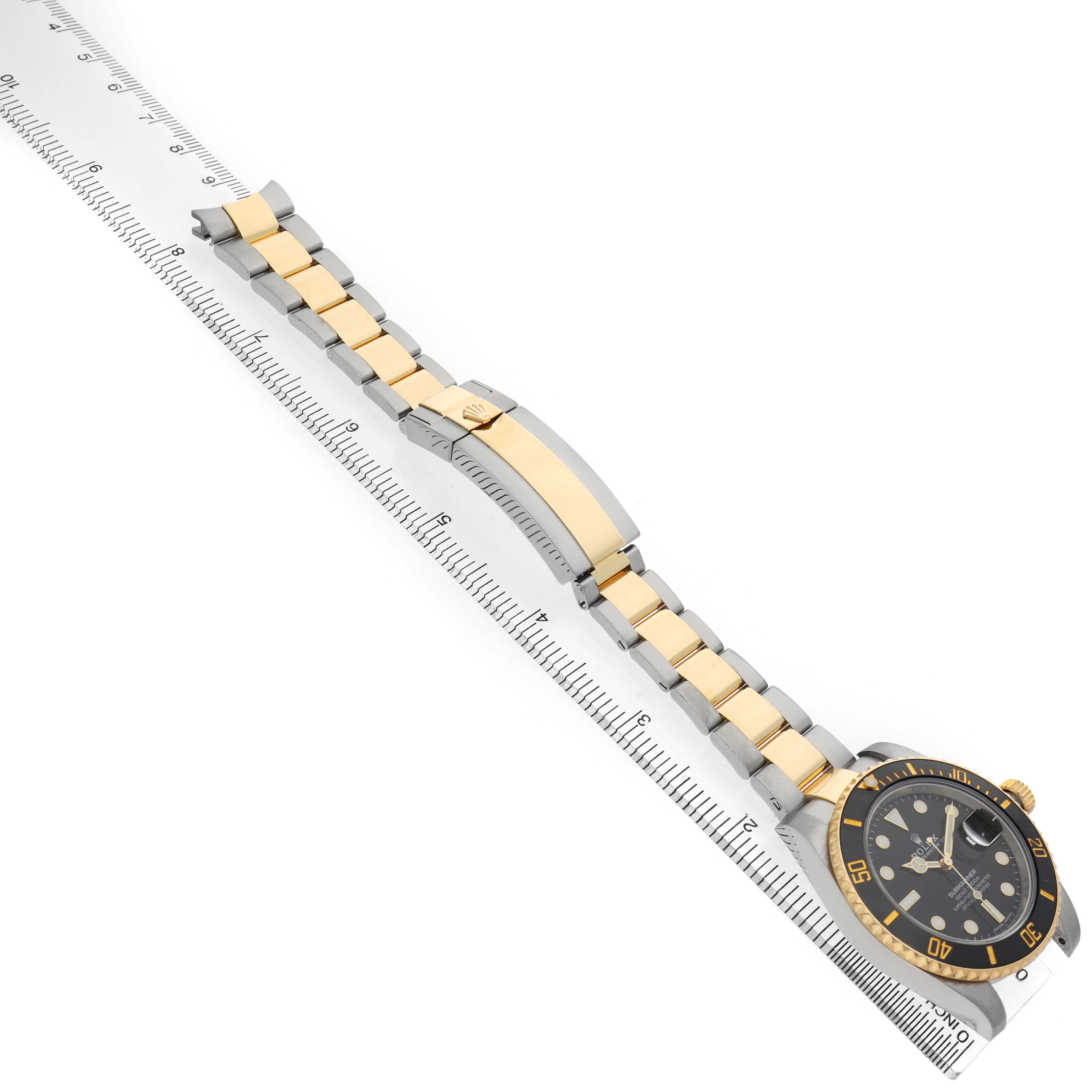 The Rolex Submariner 116613LN Men's Steel and Gold (two tone) Black Dial watch is shown at an angle highlighting its dial, bezel, and two-tone bracelet alongside a measuring ruler.