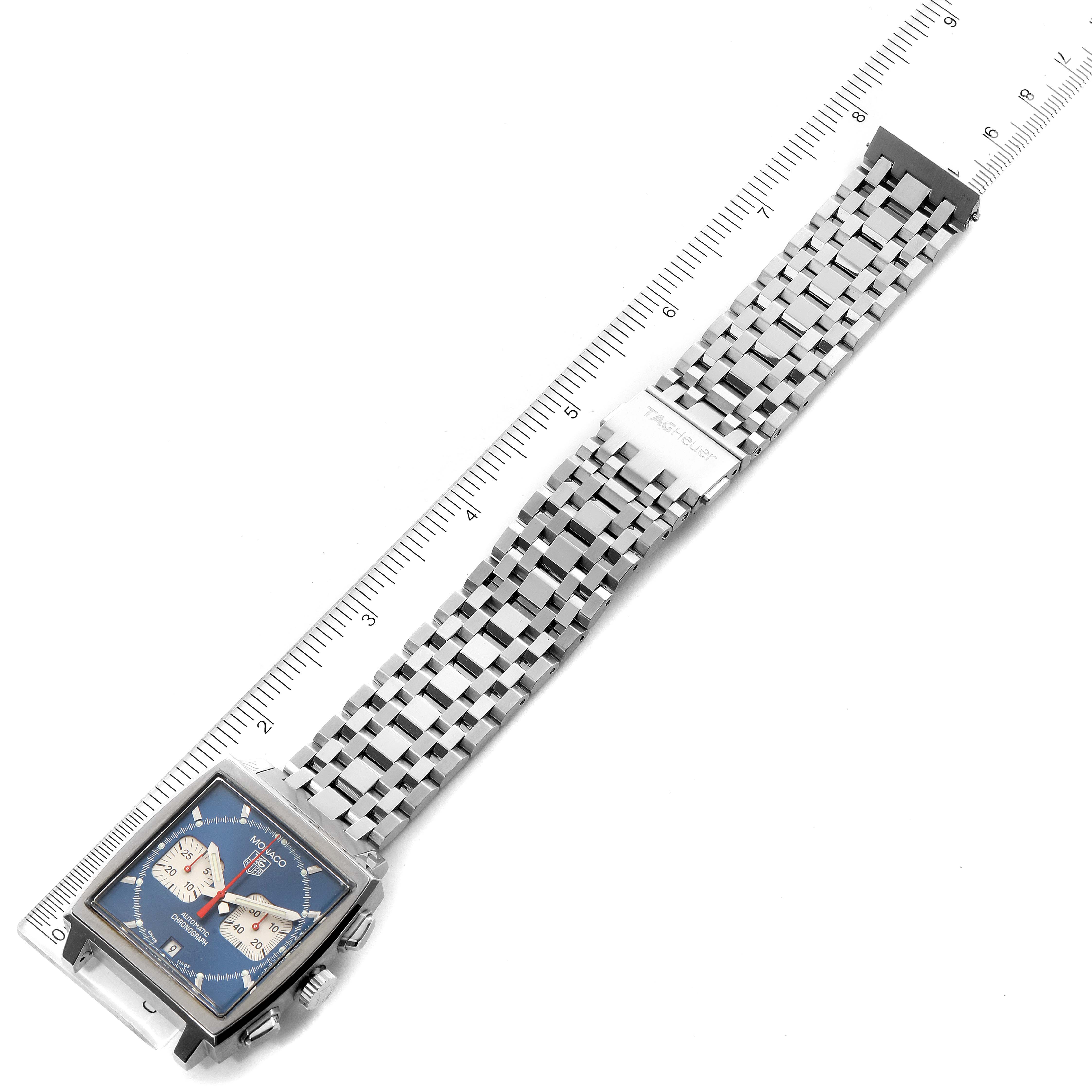 The image shows a top-down view of a Tag Heuer Monaco CW2113.BA0780 Men's Stainless Steel Blue Dial CW2113.BA0780 Men's Stainless Steel Blue Dial watch with its strap and a measuring ruler.
