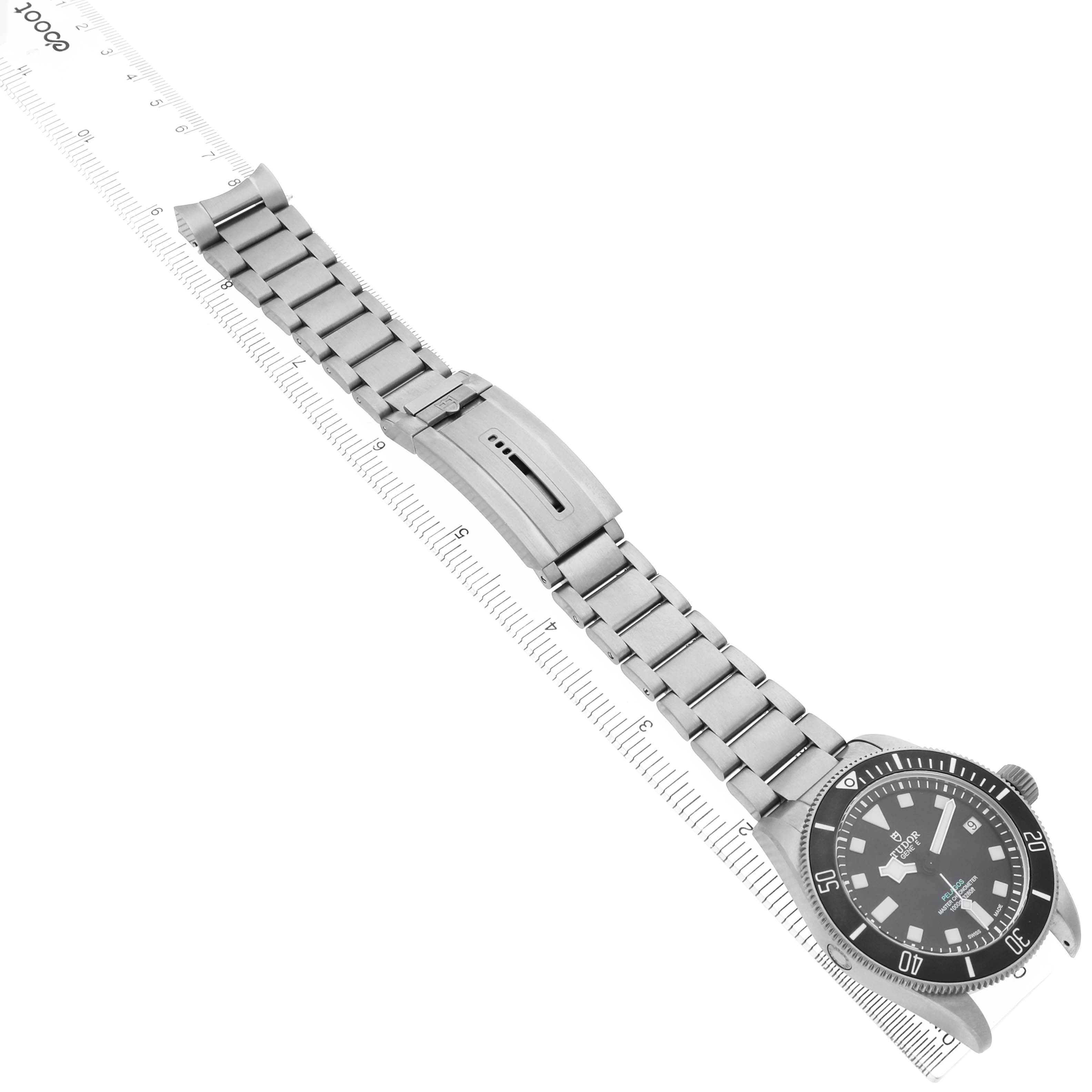 The Tudor Pelagos M2543C1A7NU-0001 Men's Titanium Black Dial watch is shown from a top view, displaying the full bracelet, clasp, and watch face alongside a measuring ruler.