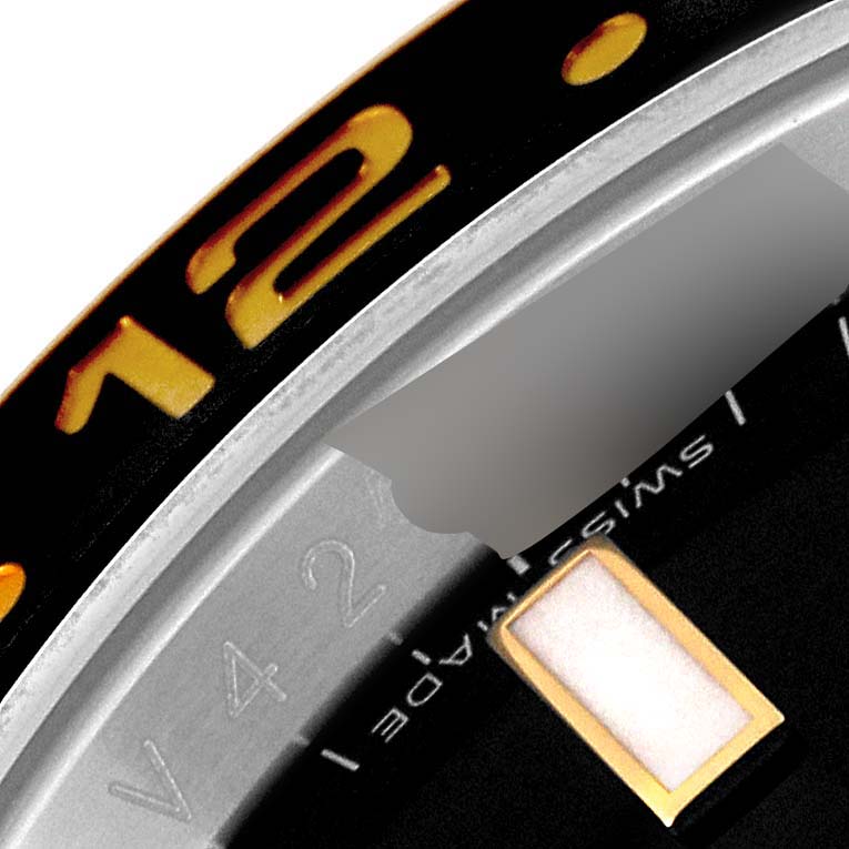 This close-up image shows part of the bezel, the "12" marker, and part of the dial of a Rolex GMT-Master 116713 Men's Steel and Gold (two tone) Black Dial 116713 Men's Steel and Gold (two tone) Black Dial watch.