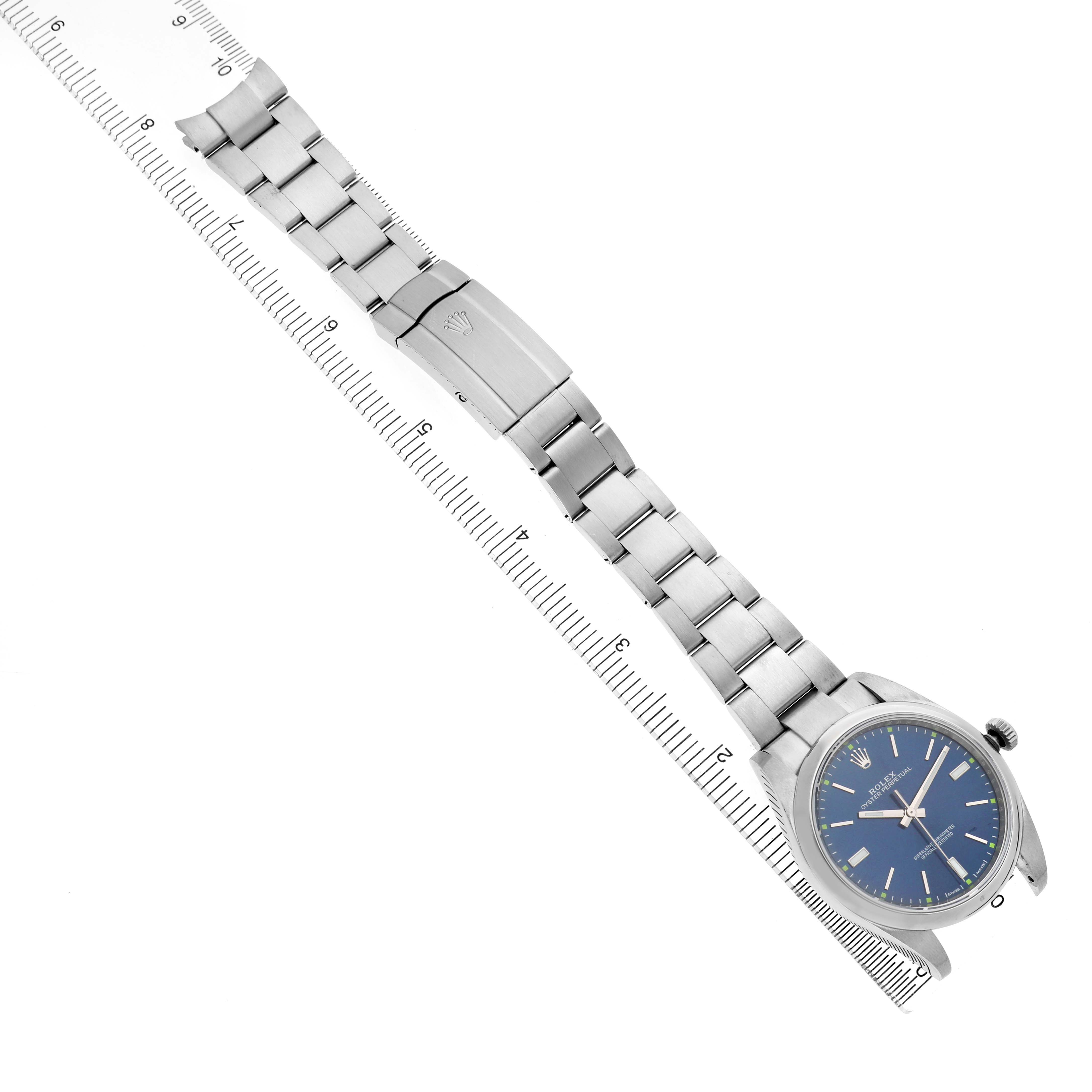 The image shows a Rolex Oyster Perpetual 114300 Men's Stainless Steel Blue Dial watch at a diagonal angle, displaying the face, bezel, bracelet, and deployment clasp.