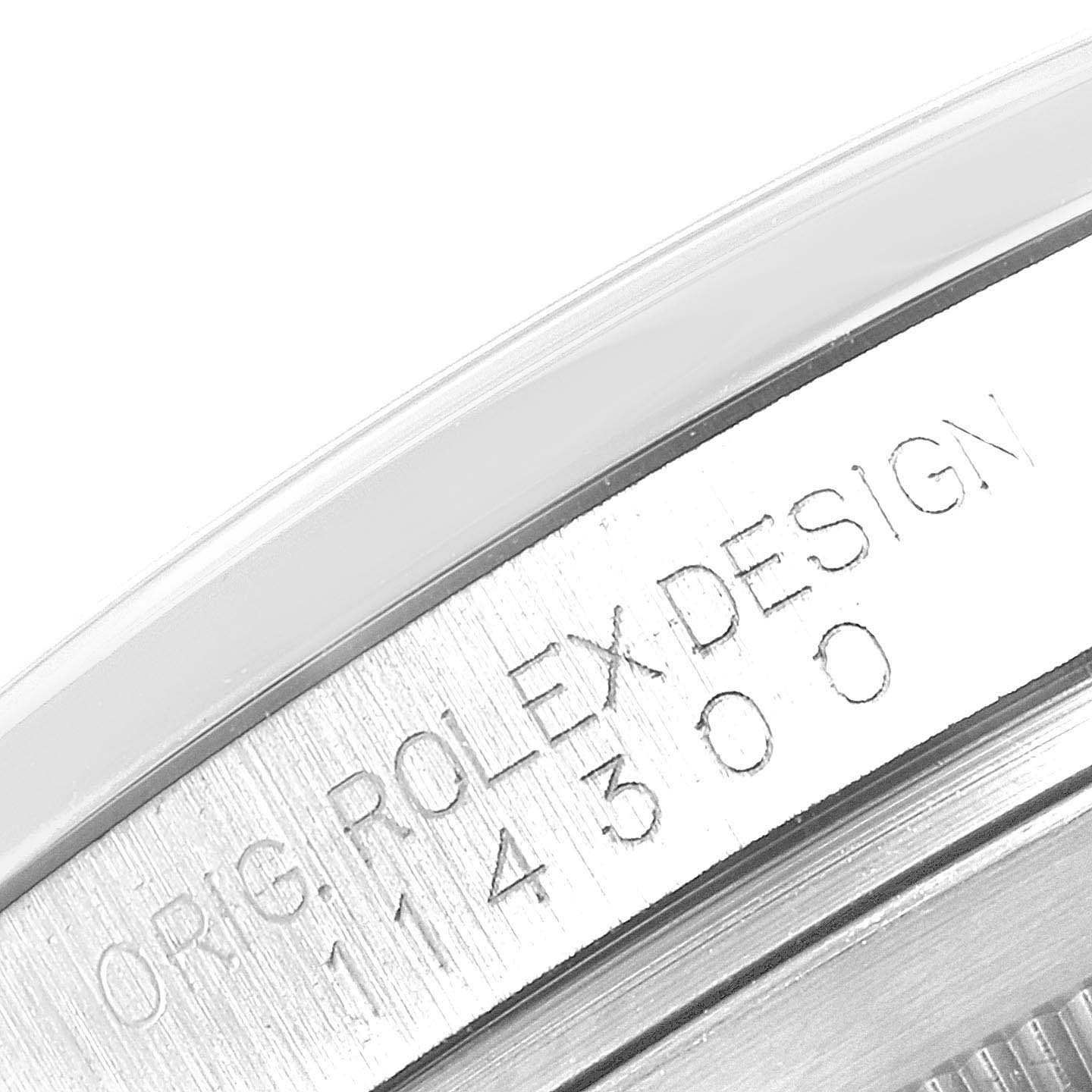 The image shows an engraving on the side of the Rolex Oyster Perpetual 114300 Men's Stainless Steel Blue Dial's case, highlighting "ORIG. ROLEX DESIGN" and model number.