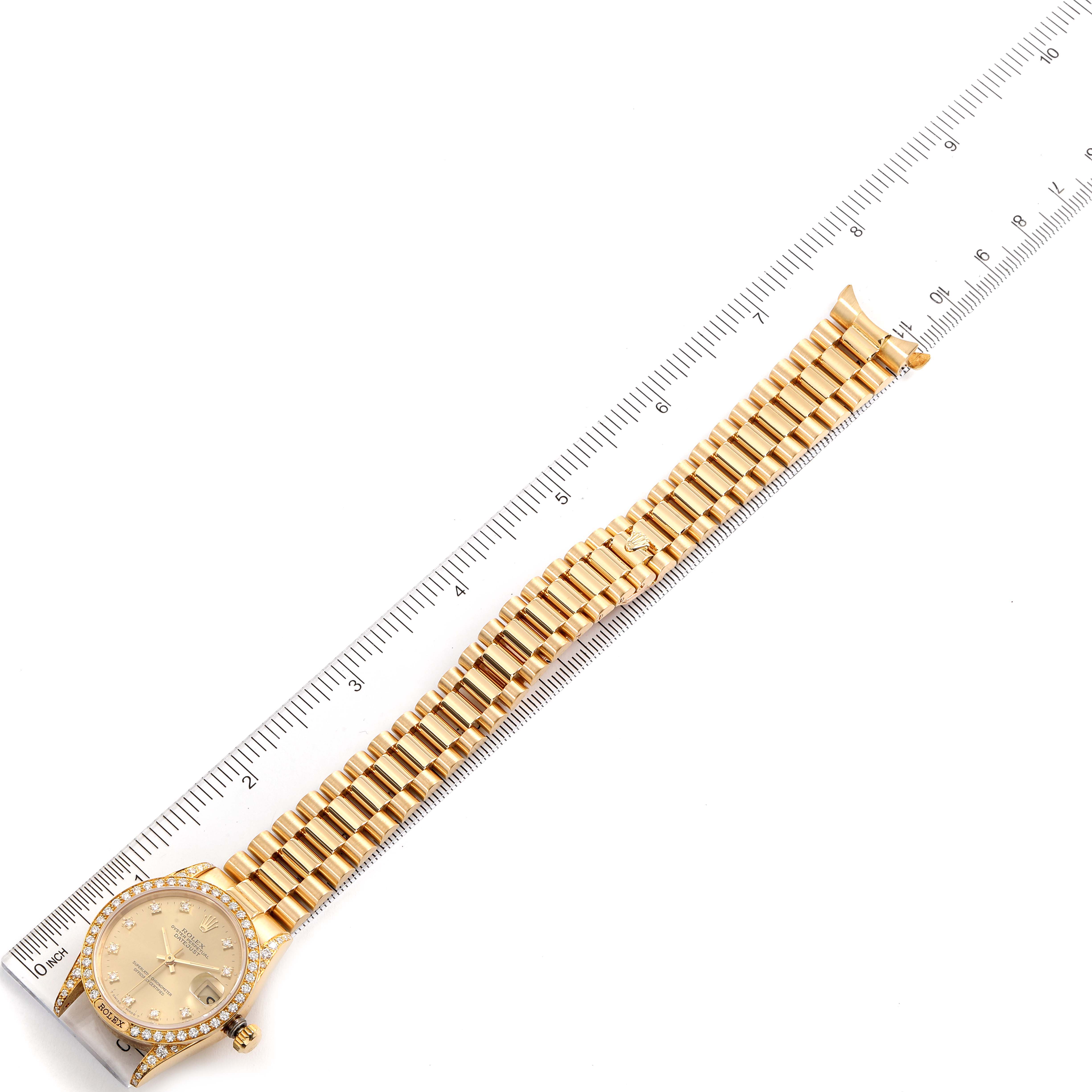 The image shows a Rolex President 69158 Women
s Yellow Gold Champagne Dial 69158 Women
s Yellow Gold Champagne Dial model watch laid flat next to a ruler, highlighting its dial, bezel, and bracelet.