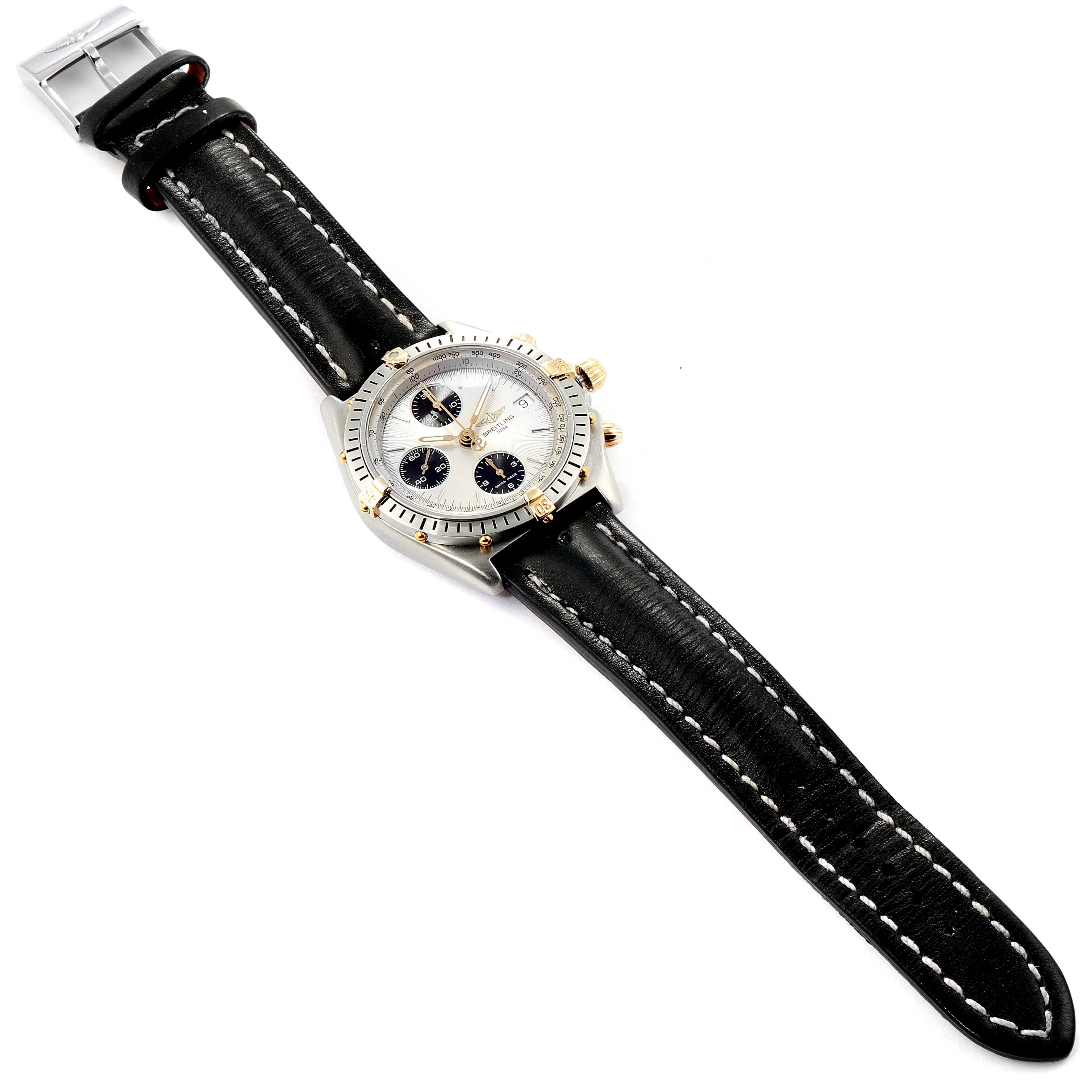 The Breitling Chronomat B13050 Men's Steel and Gold (two tone) Silver Dial B13050 Men's Steel and Gold (two tone) Silver Dial watch is shown from a slight top-down angle, displaying the entire face, leather strap, and deployment clasp.