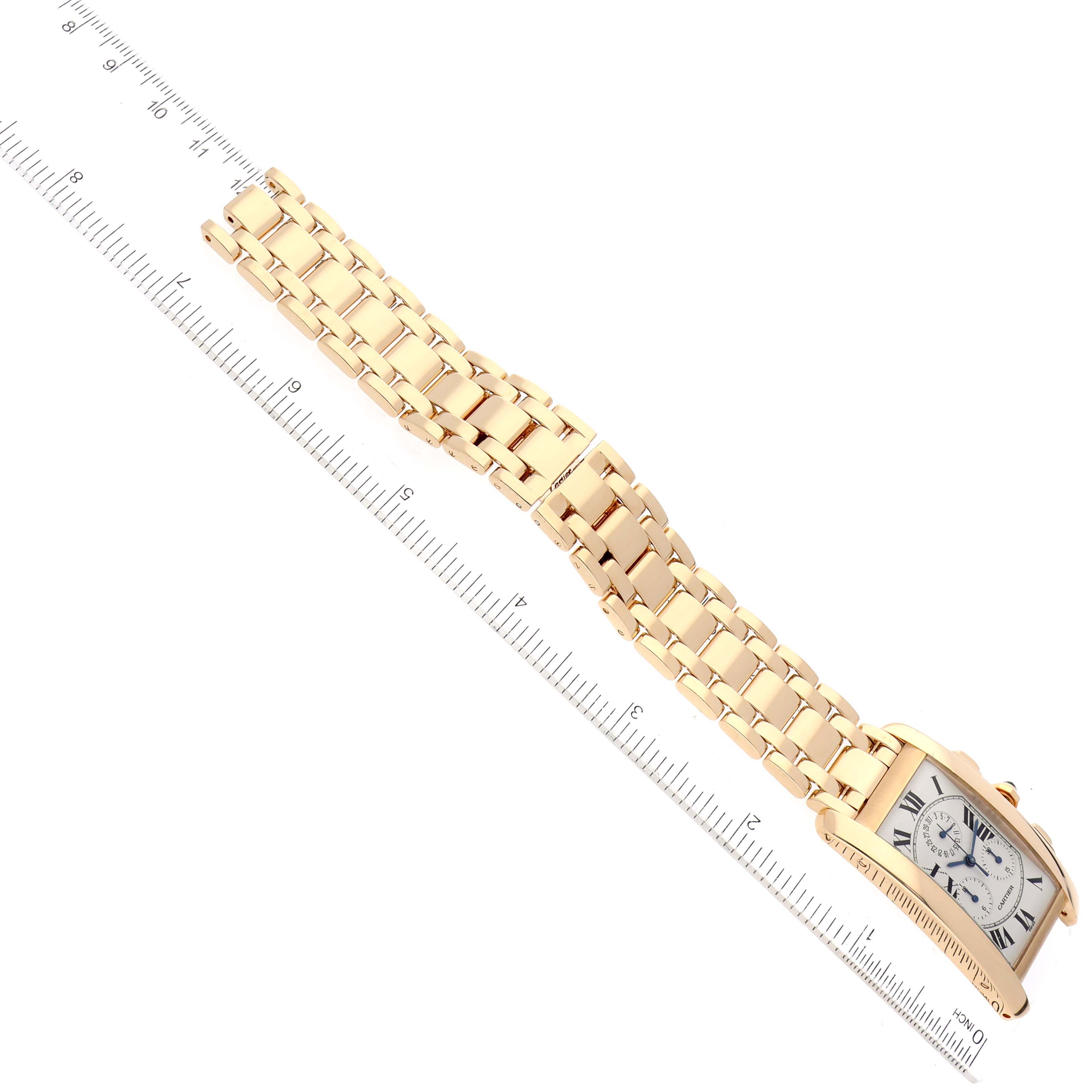 The image shows a Cartier Tank Americaine W26011K2 Men
s Yellow Gold Silver Dial W26011K2 Men
s Yellow Gold Silver Dial watch and its gold bracelet at a diagonal angle, with a ruler placed alongside for scale.