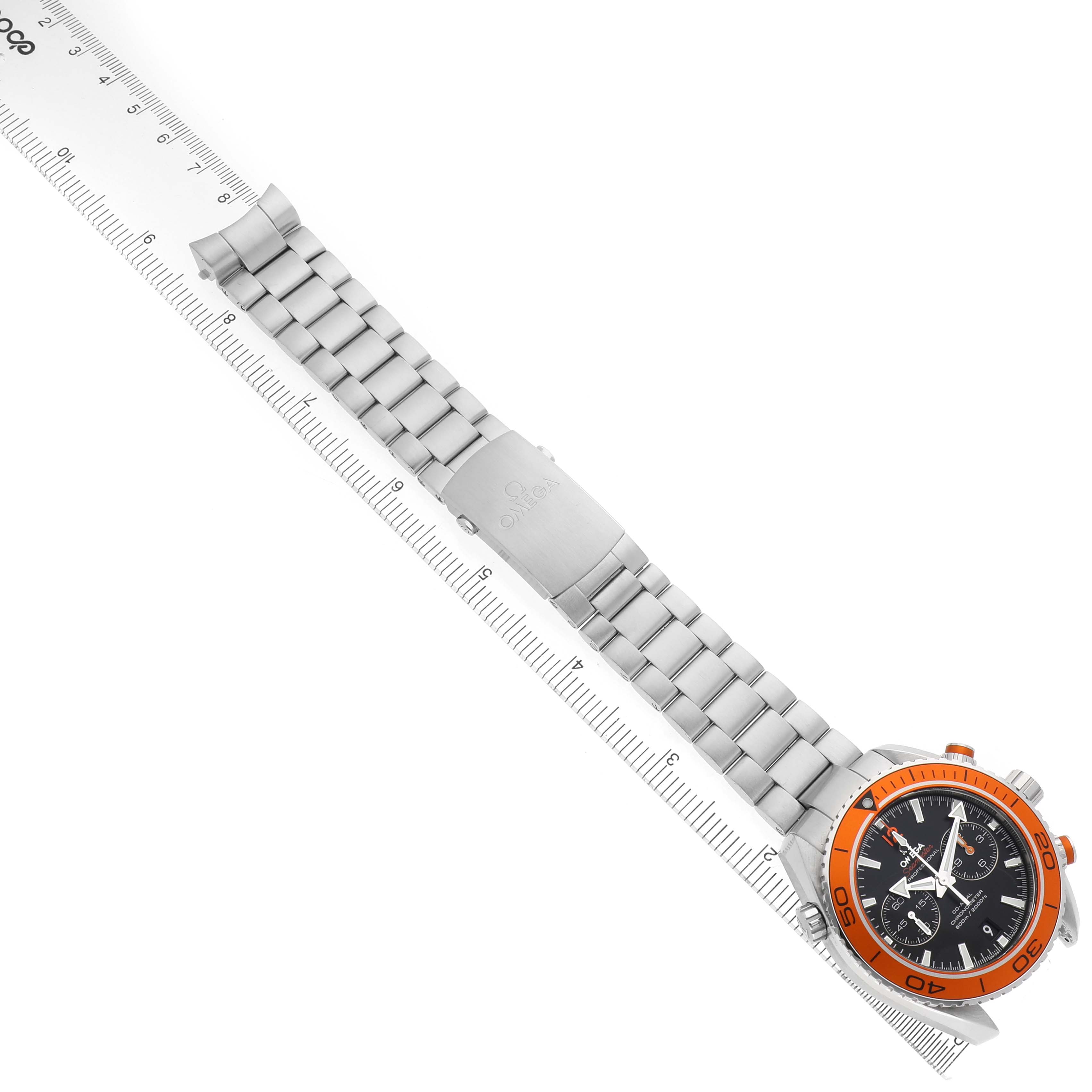 The Omega Planet Ocean 232.30.46.51.01.002 Men's Stainless Steel Black Dial watch is shown from a top-down angle, highlighting the orange bezel, black dial, and metal bracelet against a ruler.