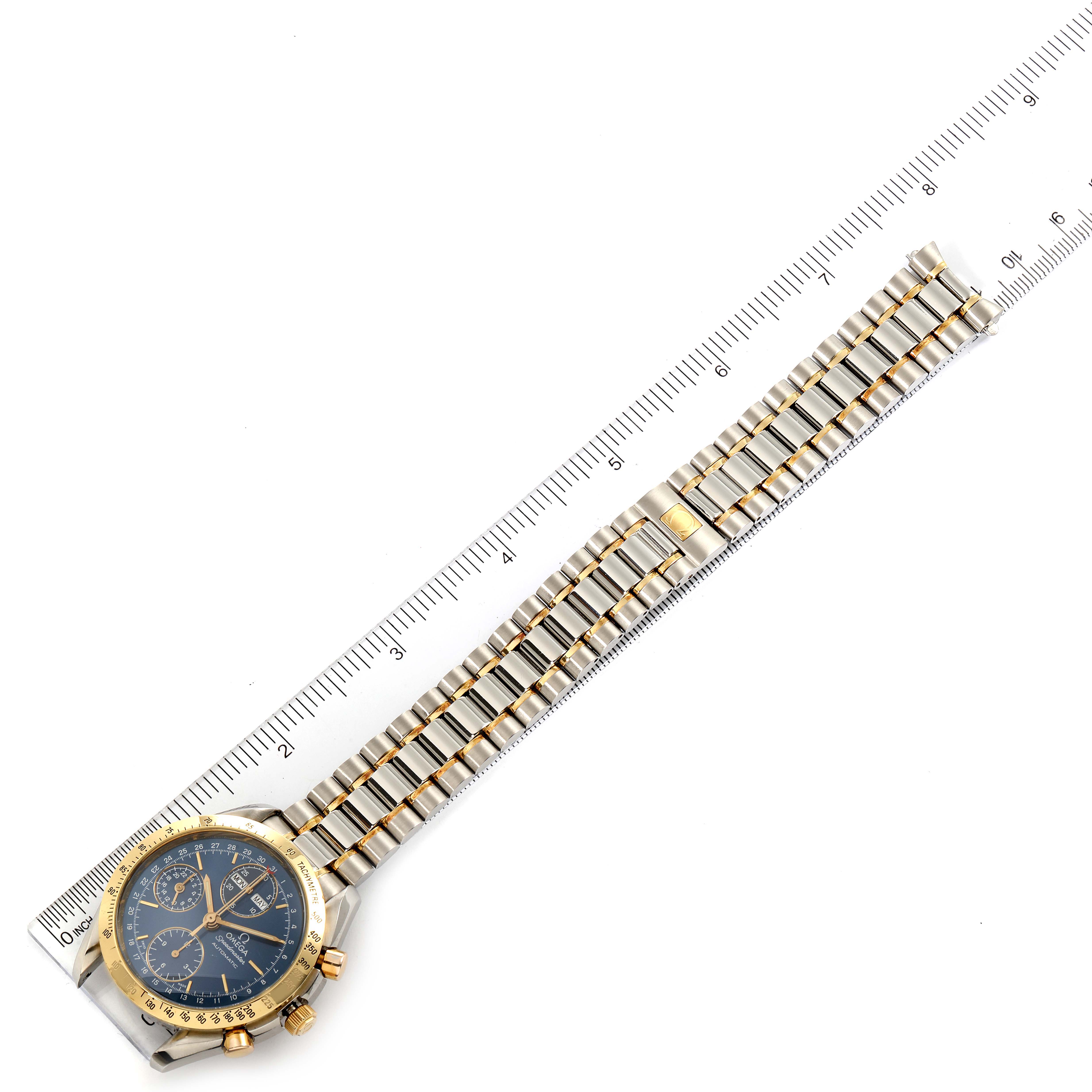 The image shows an Omega Speedmaster 3321.80.00 Men's Steel and Gold (two tone) Blue Dial 3321.80.00 Men's Steel and Gold (two tone) Blue Dial watch with a ruler, displaying its dial, bezel, and entire bracelet from a slight overhead angle.