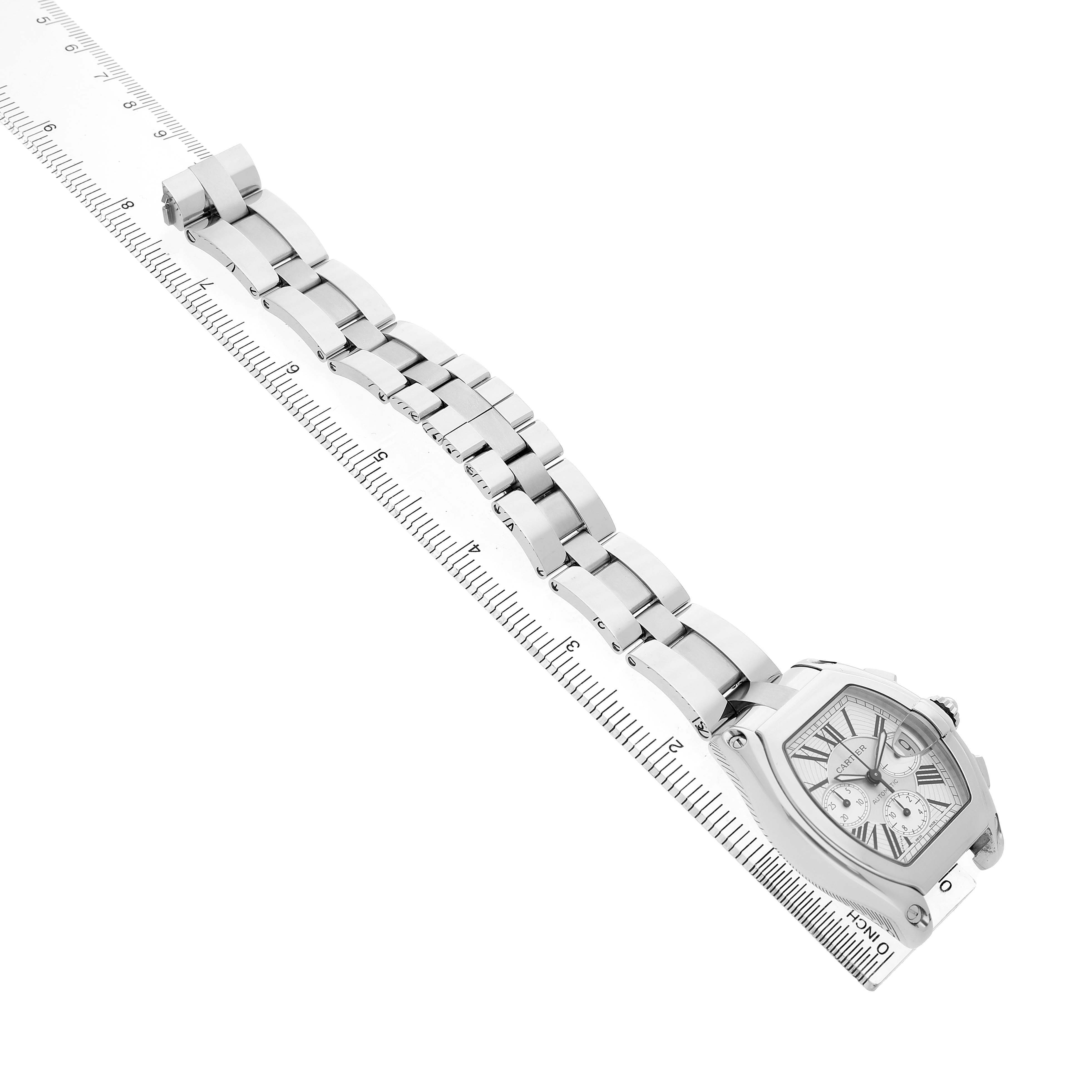 The Cartier Roadster W62019X6 Men's Stainless Steel Silver Dial watch is shown at a tilted angle, displaying the dial and full bracelet, with a ruler alongside it.