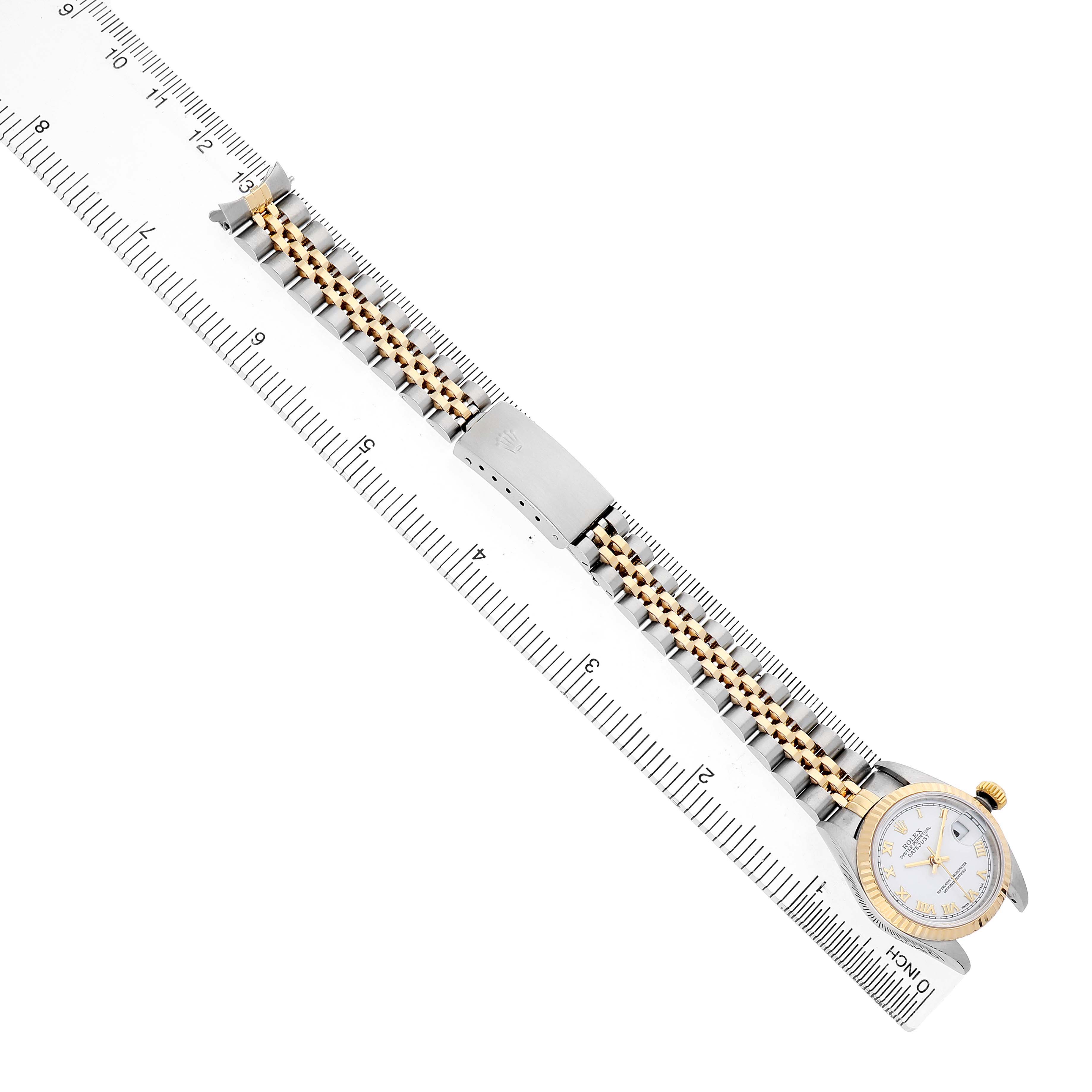 The Rolex Datejust 79173 Women's Stainless Steel White Dial watch is shown from an overhead angle, displaying its dial, bezel, and metal bracelet alongside a ruler.
