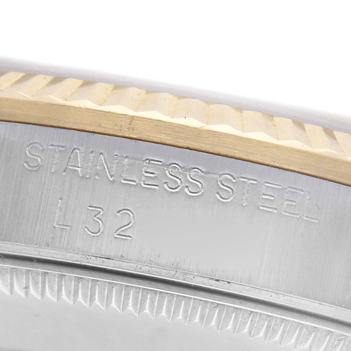 The image shows a close-up of the stainless steel and gold bezel edge of a mid-size Rolex watch.