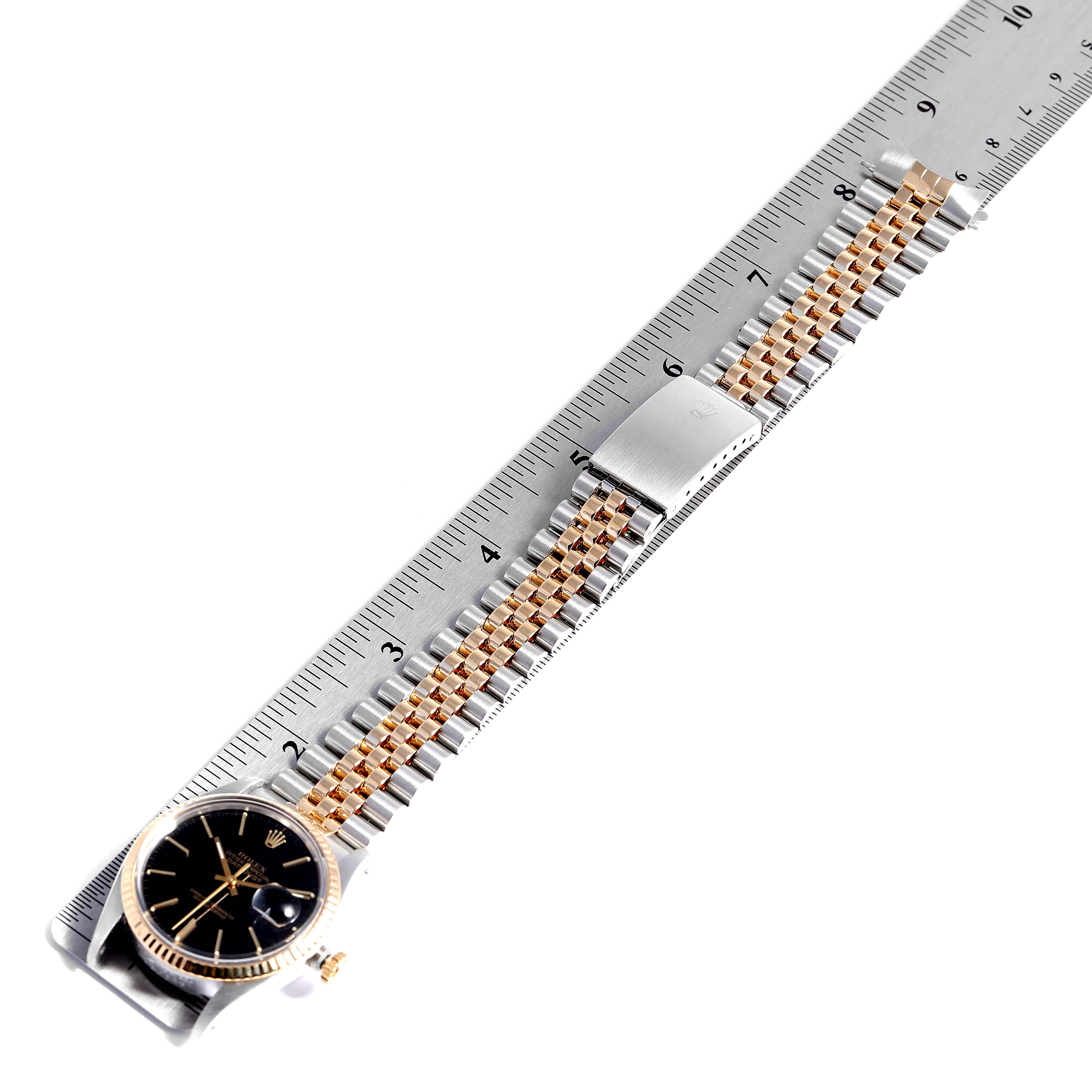 The image shows a Rolex Datejust 27465 Men
s Steel and Gold (two tone) Black Dial 27465 Men
s Steel and Gold (two tone) Black Dial watch laid flat on a ruler, displaying the dial, case, and two-tone jubilee bracelet.