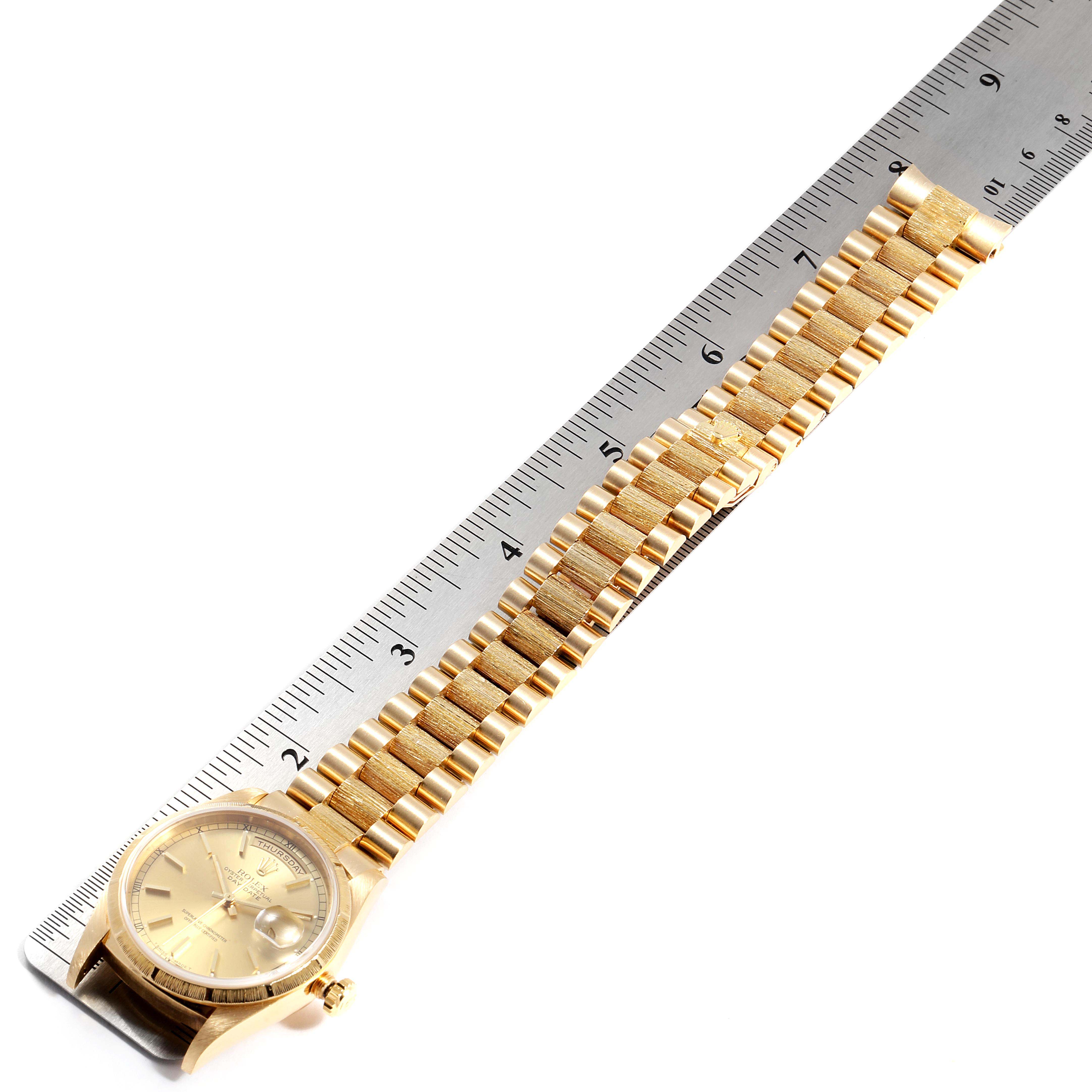 The Rolex President 18248 Men
s Yellow Gold Champagne Dial 18248 Men
s Yellow Gold Champagne Dial model watch is shown flat, alongside a ruler, displaying its face and gold bracelet.