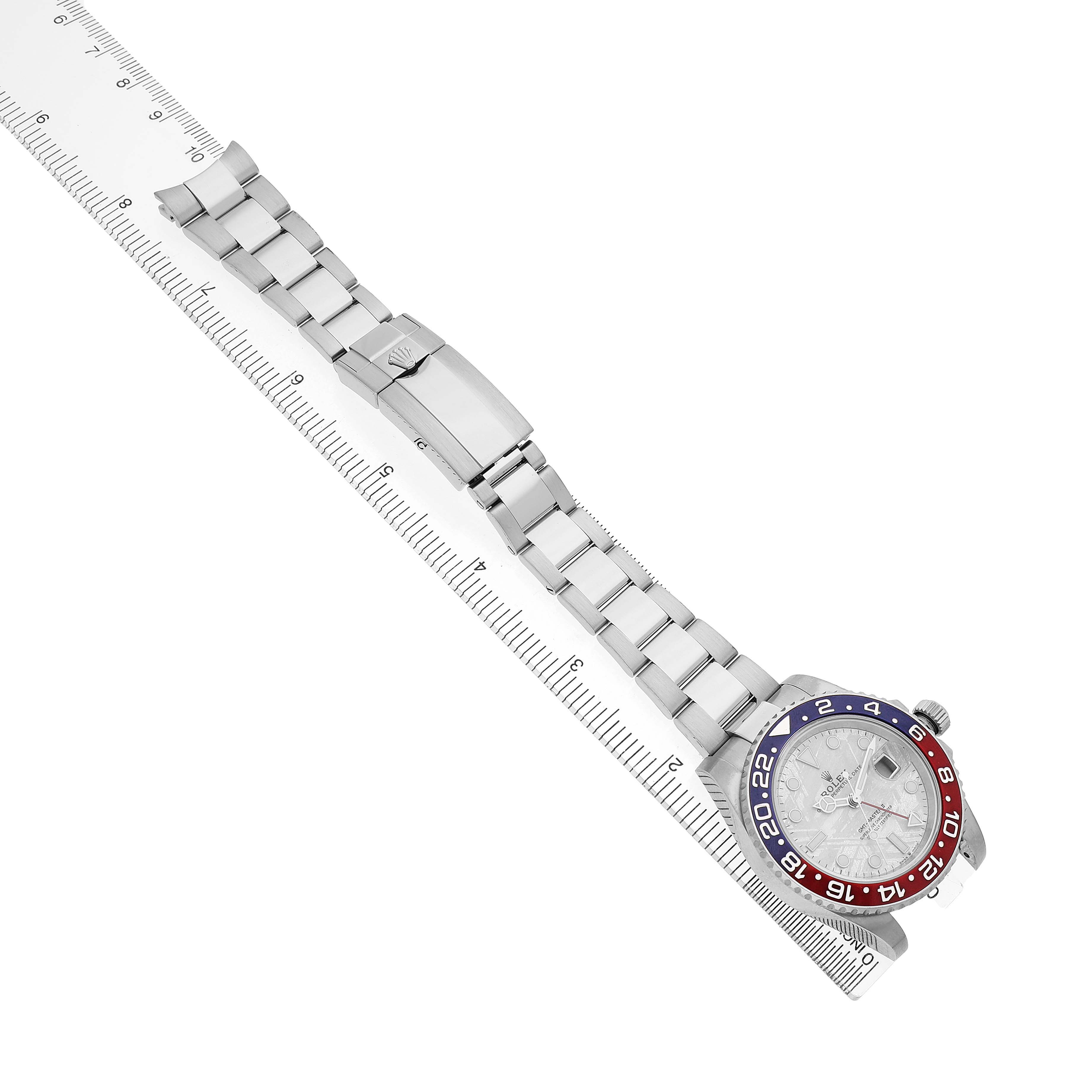 The Rolex GMT-Master 126719BLRO Men's White Gold Silver Dial watch is shown from a top view, displaying the bracelet, clasp, and bezel with a ruler beside it.