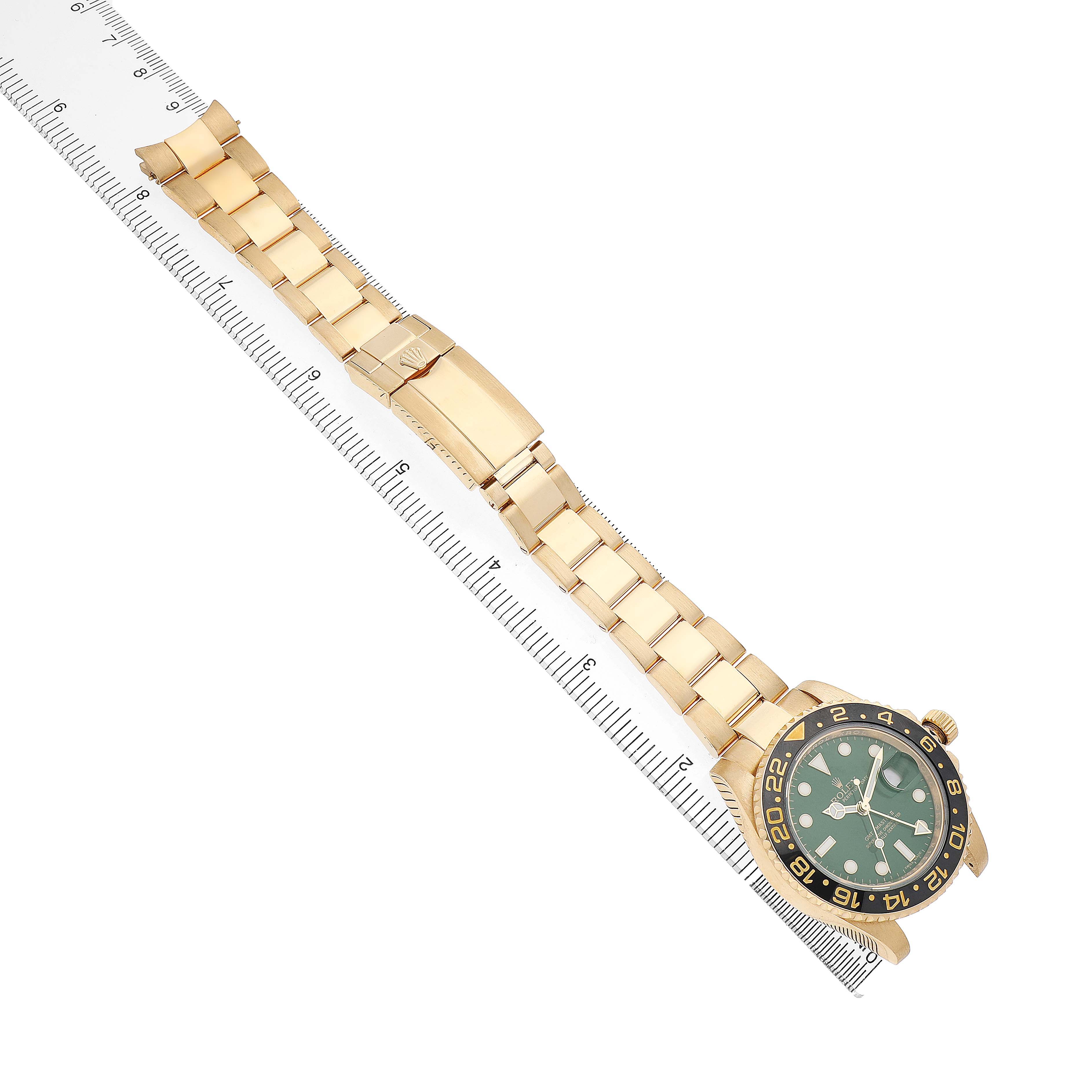 The Rolex GMT-Master 116718 Men's Yellow Gold Green Dial watch is shown from a top-down angle, displaying the full bracelet and watch face alongside a ruler.