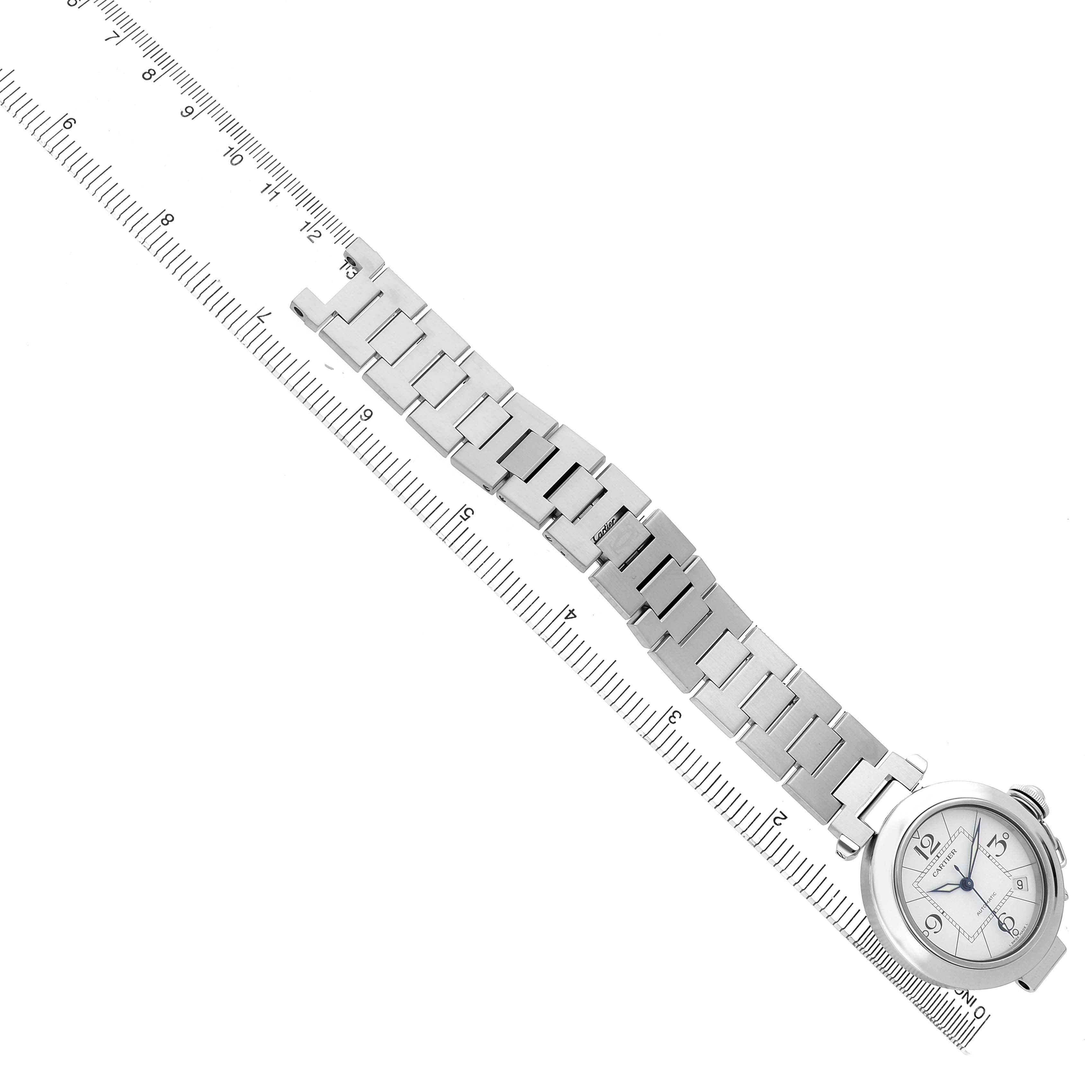 The Cartier Pasha W31074M7 Men's Stainless Steel White Dial watch is shown from a top angle, displaying its face and metal bracelet, alongside a ruler for scale.
