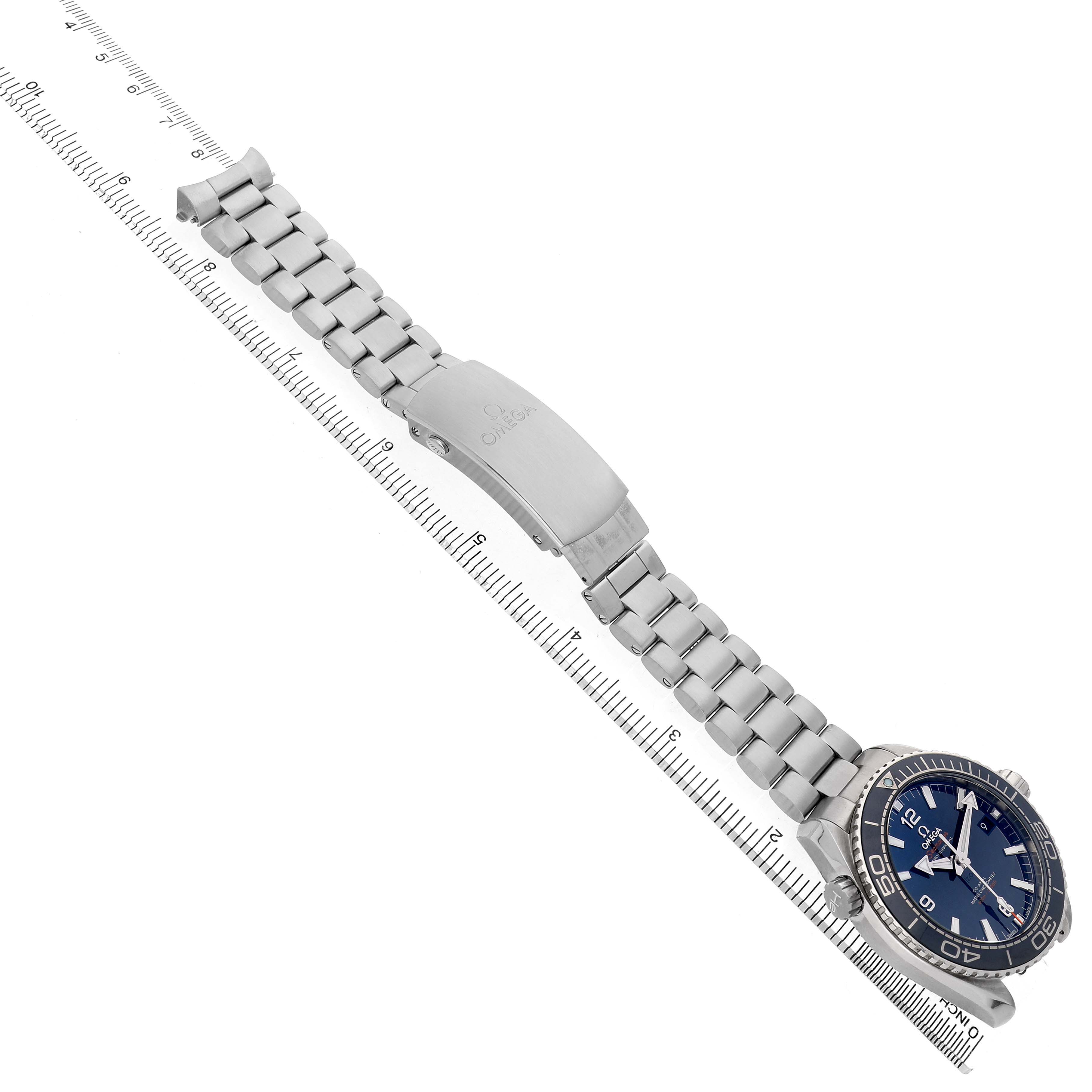 The Omega Planet Ocean 215.30.44.21.03.001 Men's Stainless Steel Blue Dial watch is shown at an angle highlighting the face, bezel, and full metal bracelet alongside a ruler.