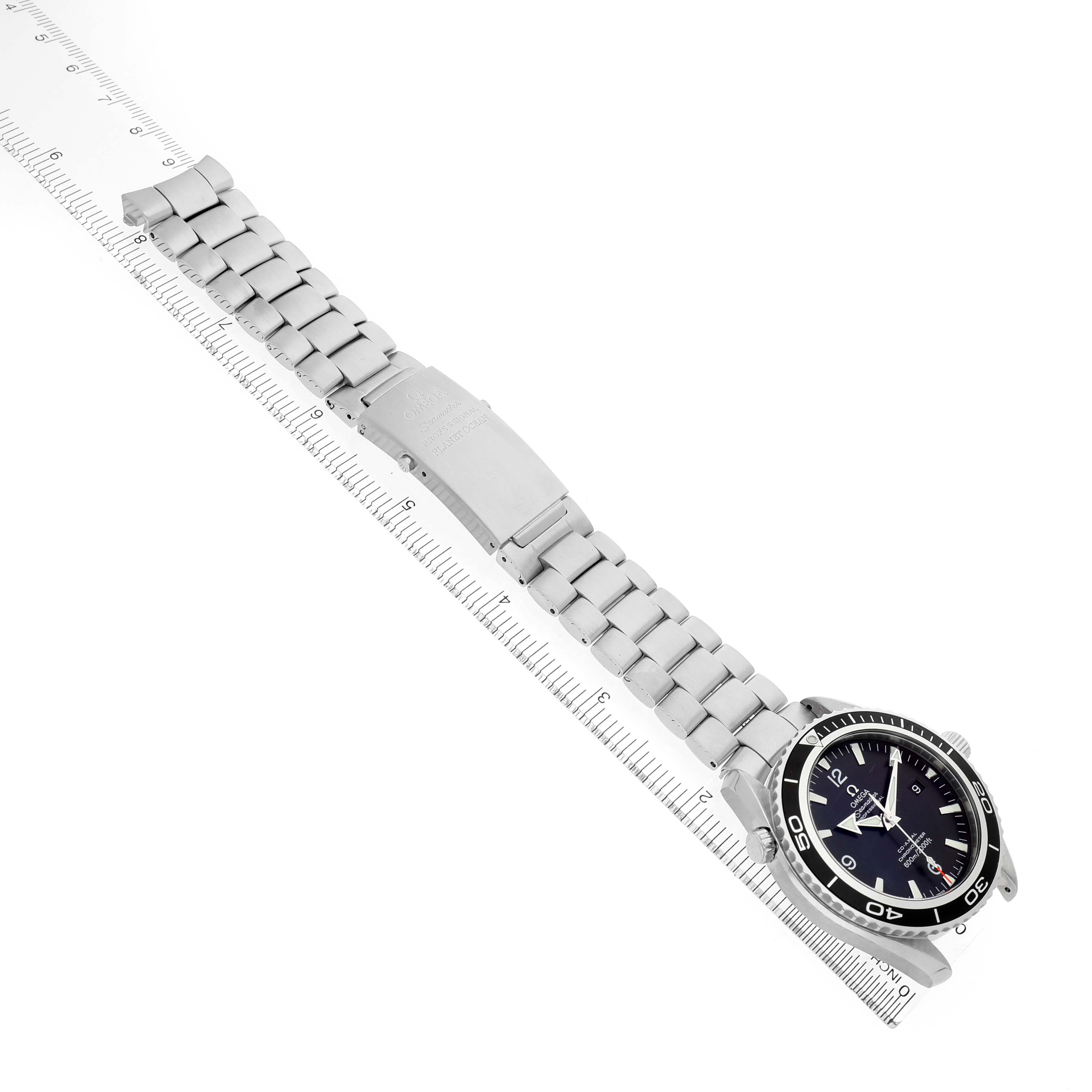 The Omega Planet Ocean 2200.50.00 Men's Stainless Steel Black Dial watch is shown at an angled side view, displaying the face, bezel, bracelet, and clasp next to a ruler.