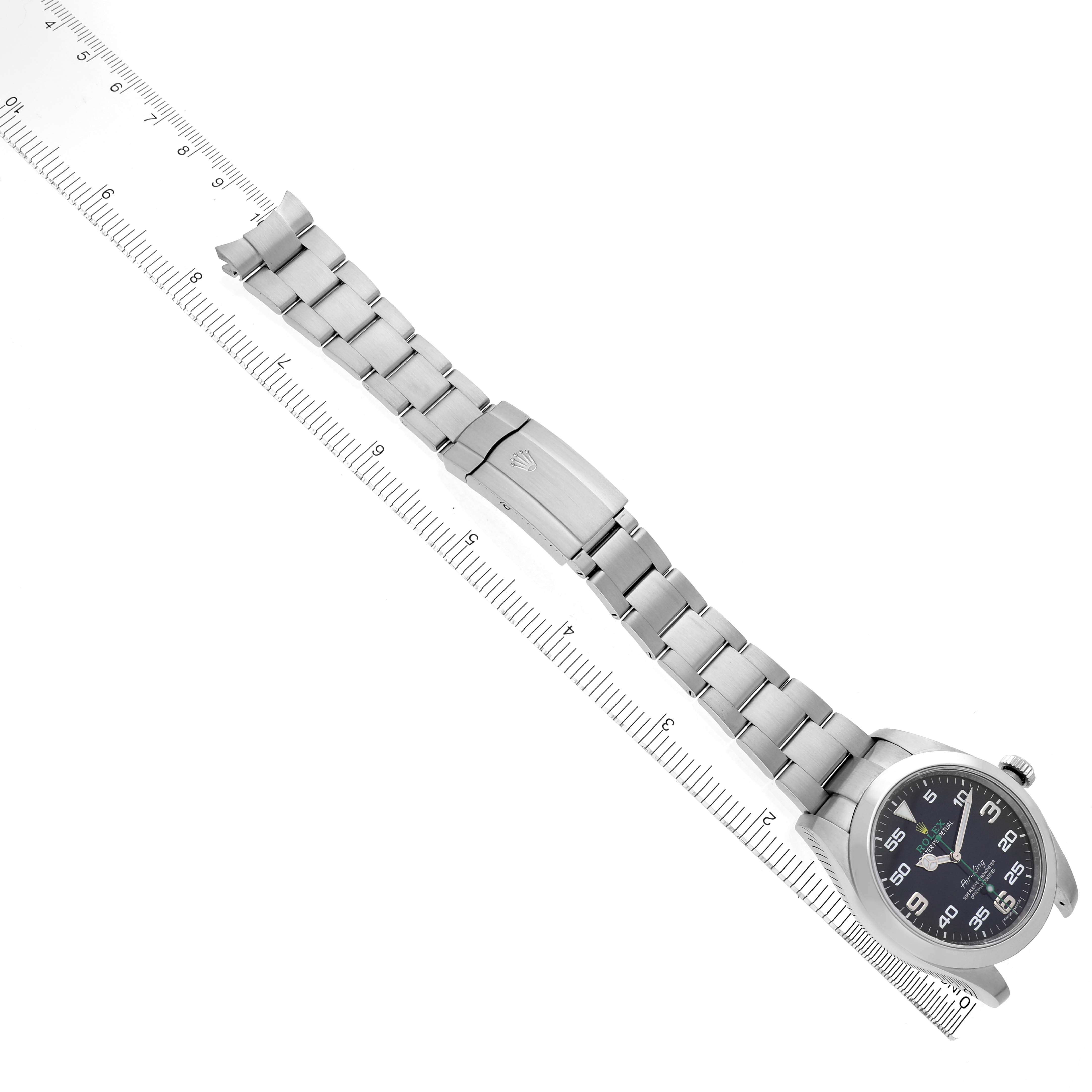 The image shows a Rolex Air-King 116900 Men's Stainless Steel Black Dial watch from a top-down angle, displaying the face, bracelet, and clasp alongside a measuring ruler.