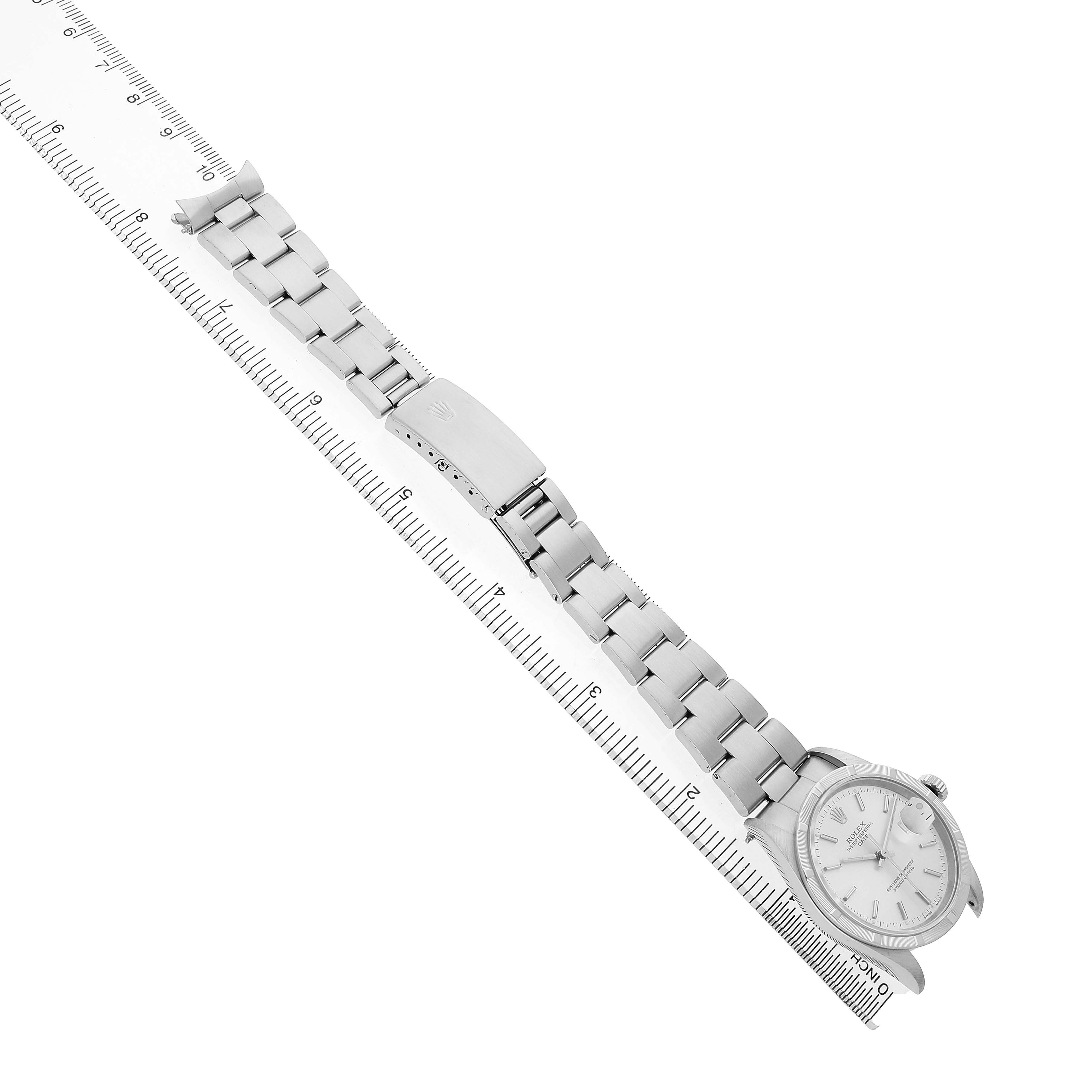 The Rolex Date 15210 Men's Stainless Steel Silver Dial watch is shown at an angle displaying the face, bracelet, and clasp, alongside a ruler for scale.