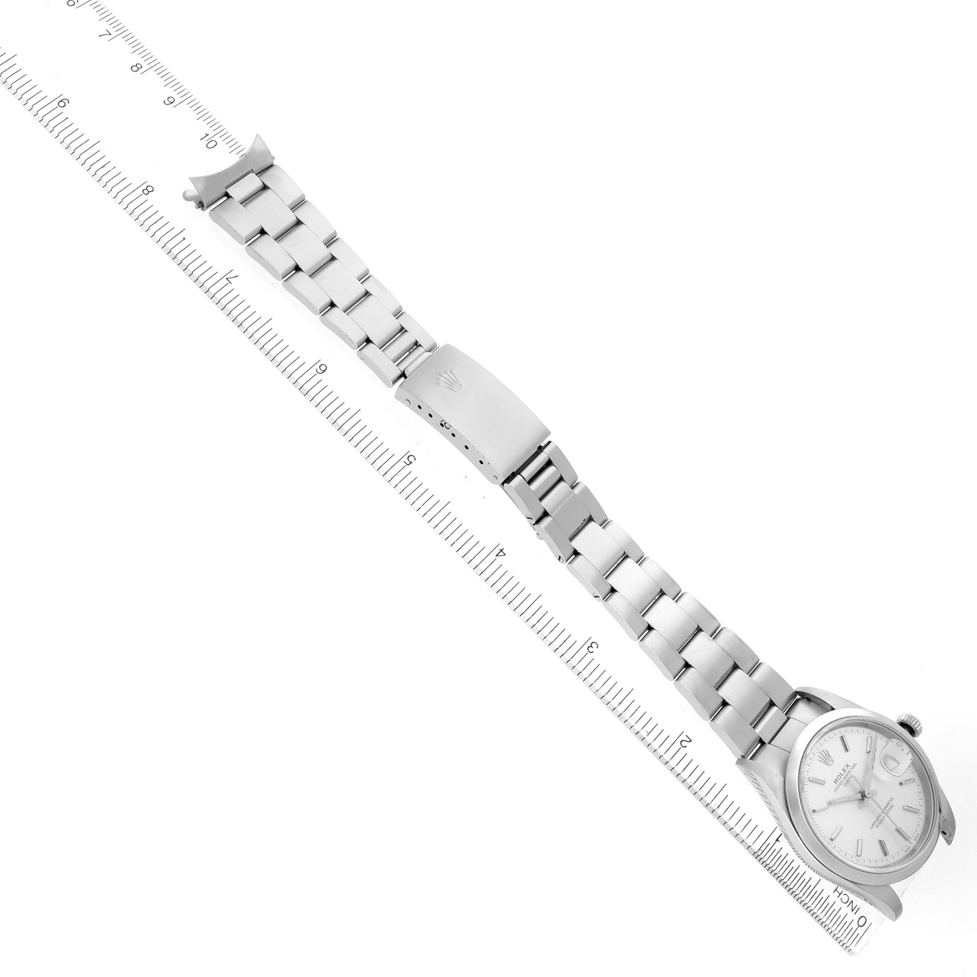 The Rolex Date 15200 Men's Stainless Steel Silver Dial watch is shown from an overhead angle, displaying its bracelet and clasp alongside a measuring scale.
