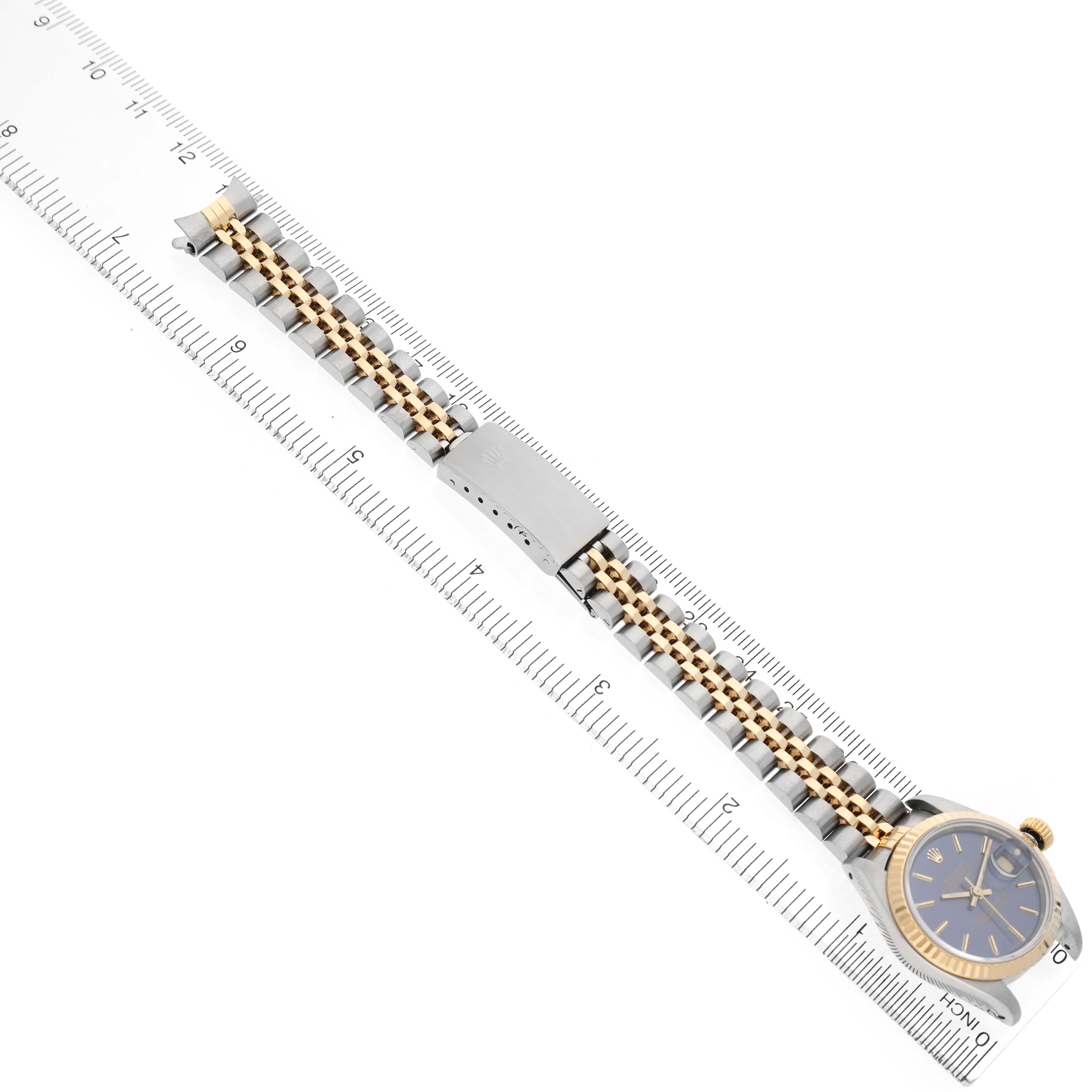 The Rolex Datejust 69173 Women's Steel and Gold (two tone) Blue Dial watch is shown diagonally, featuring its face, bezel, bracelet, and clasp next to a ruler for scale.