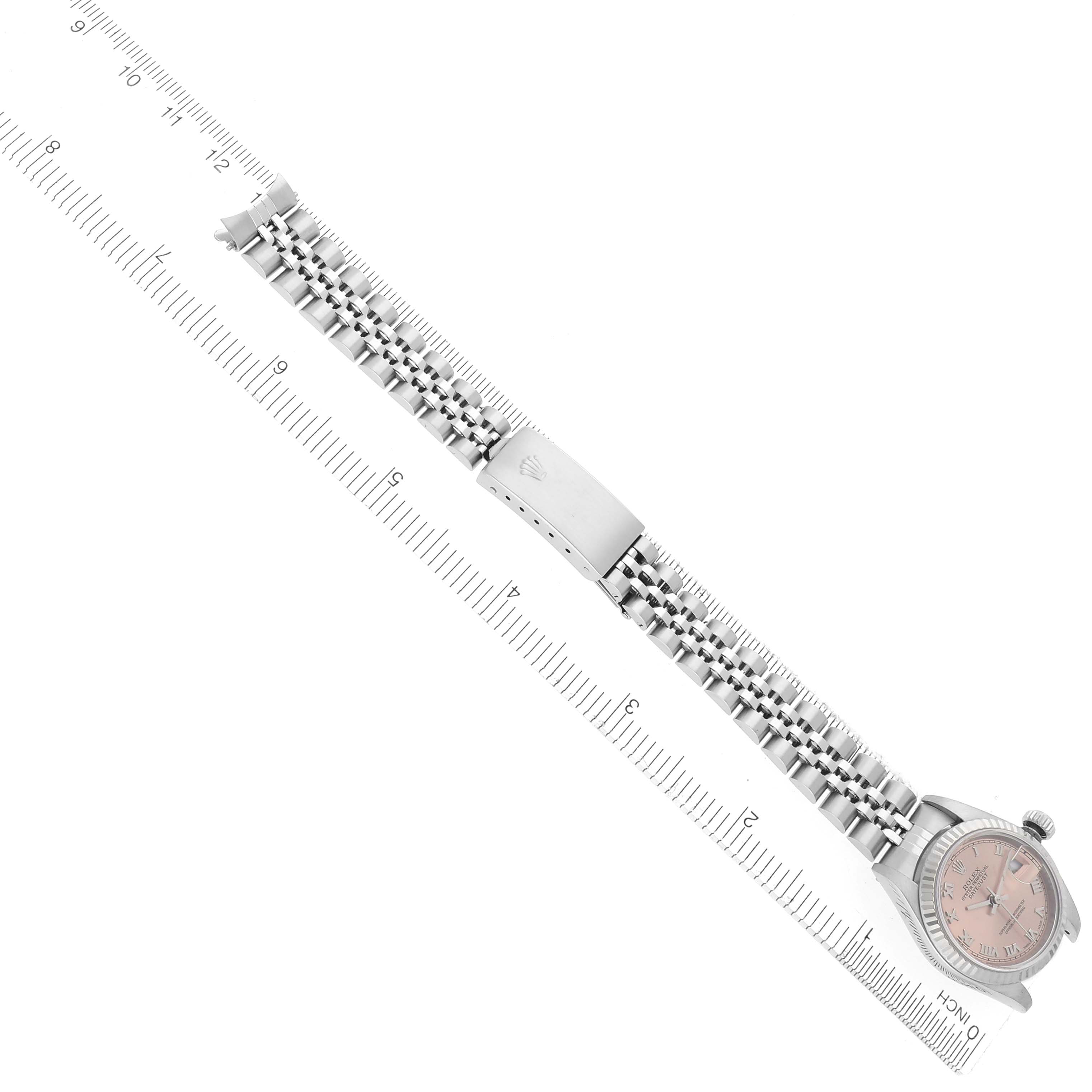 The image shows a flat-lay view of a Rolex Datejust 79174 Women
s Stainless Steel Pink Dial 79174 Women
s Stainless Steel Pink Dial watch with its bracelet fully extended alongside a ruler.