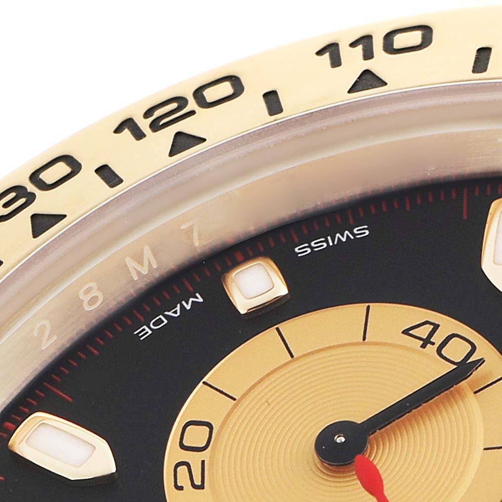 The image shows a close-up of the Rolex Daytona 116508 Men
s Yellow Gold Black Dial 116508 Men
s Yellow Gold Black Dial
s bezel and dial, featuring numerals and part of the seconds sub-dial.