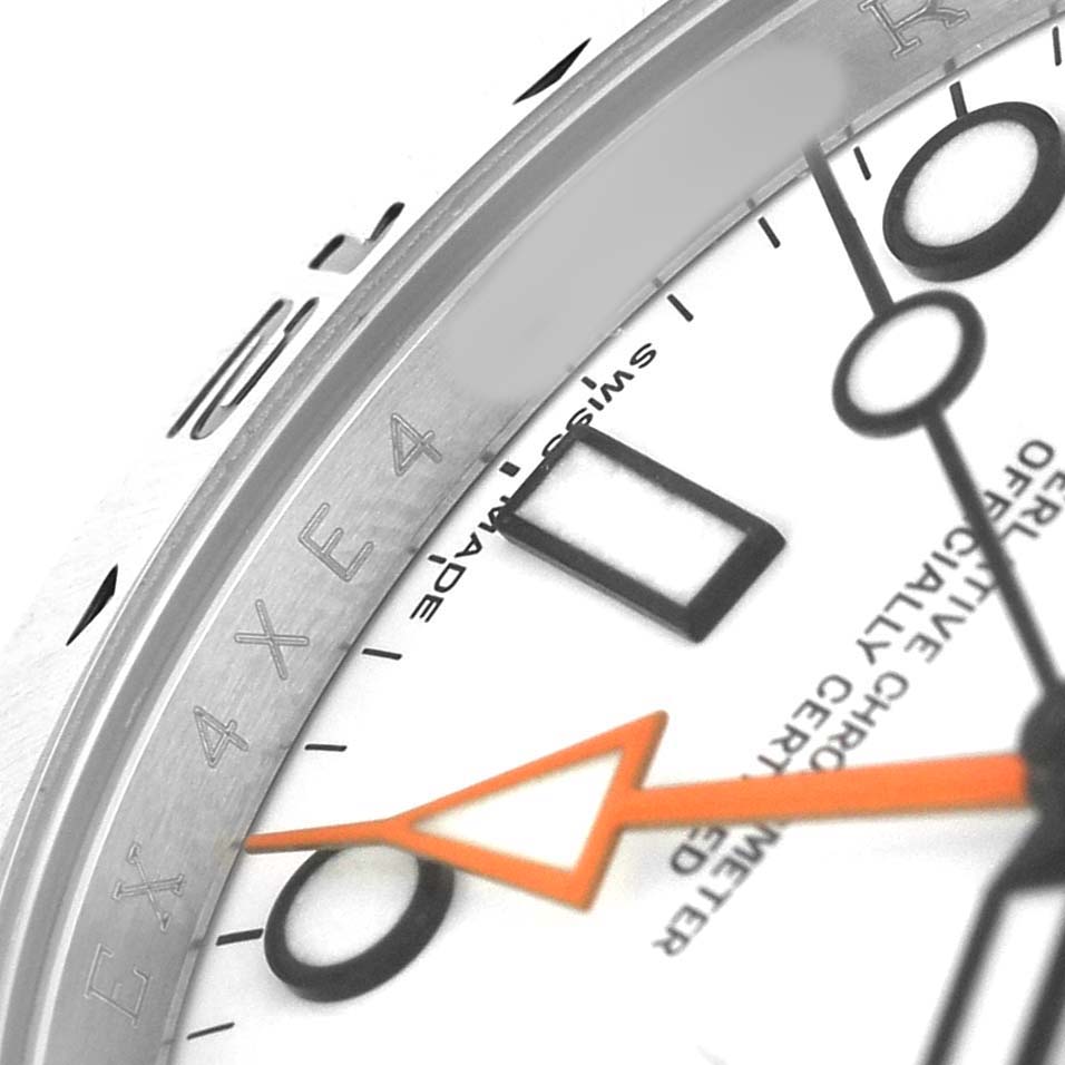 The image shows a close-up of the Rolex Explorer 216570 Men's Stainless Steel White Dial watch's bezel, dial, and orange hand from an angled view.