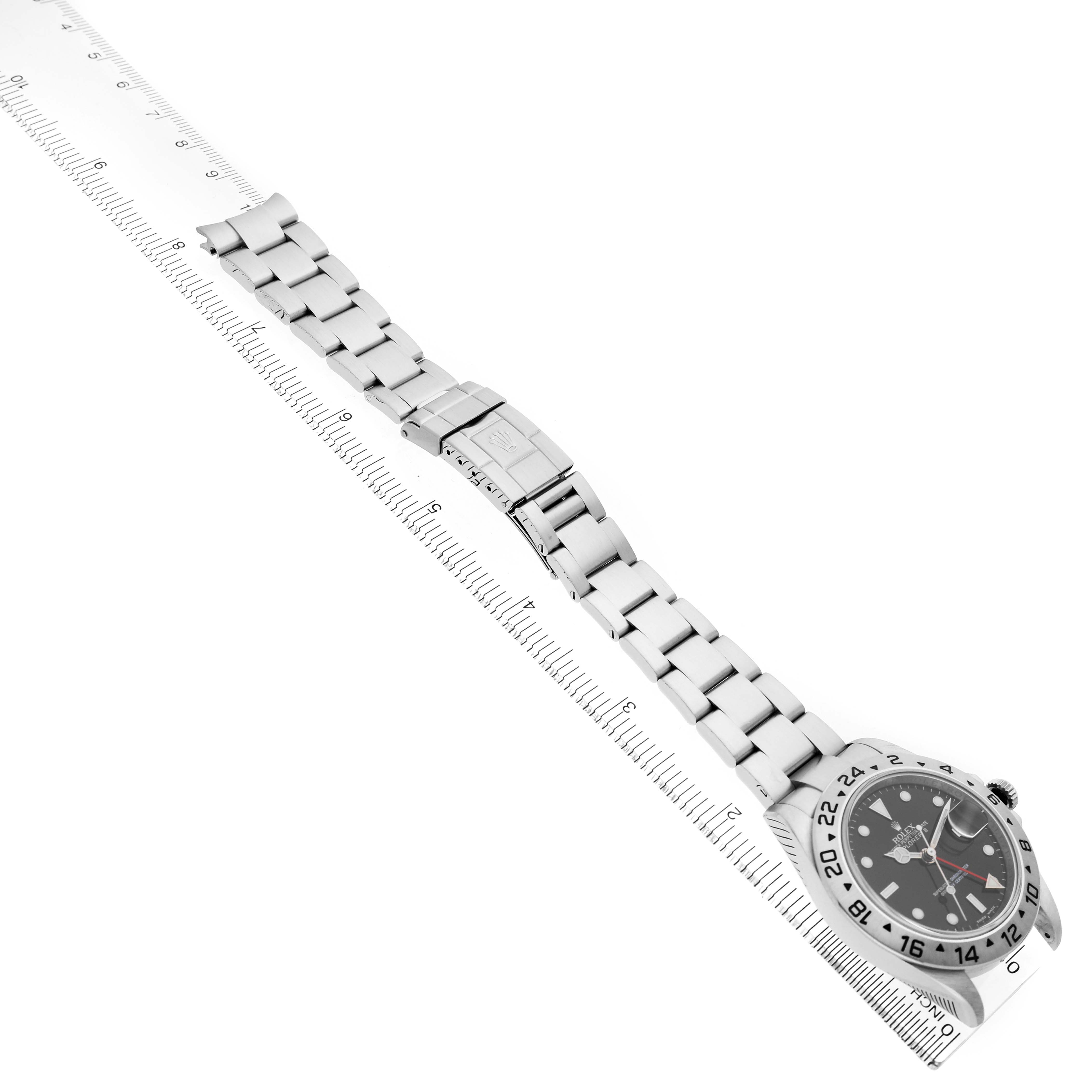 The Rolex Explorer 16570 Men's Stainless Steel Black Dial watch is shown laid flat, displaying its face, bracelet, and clasp from a slightly elevated angle alongside a ruler.