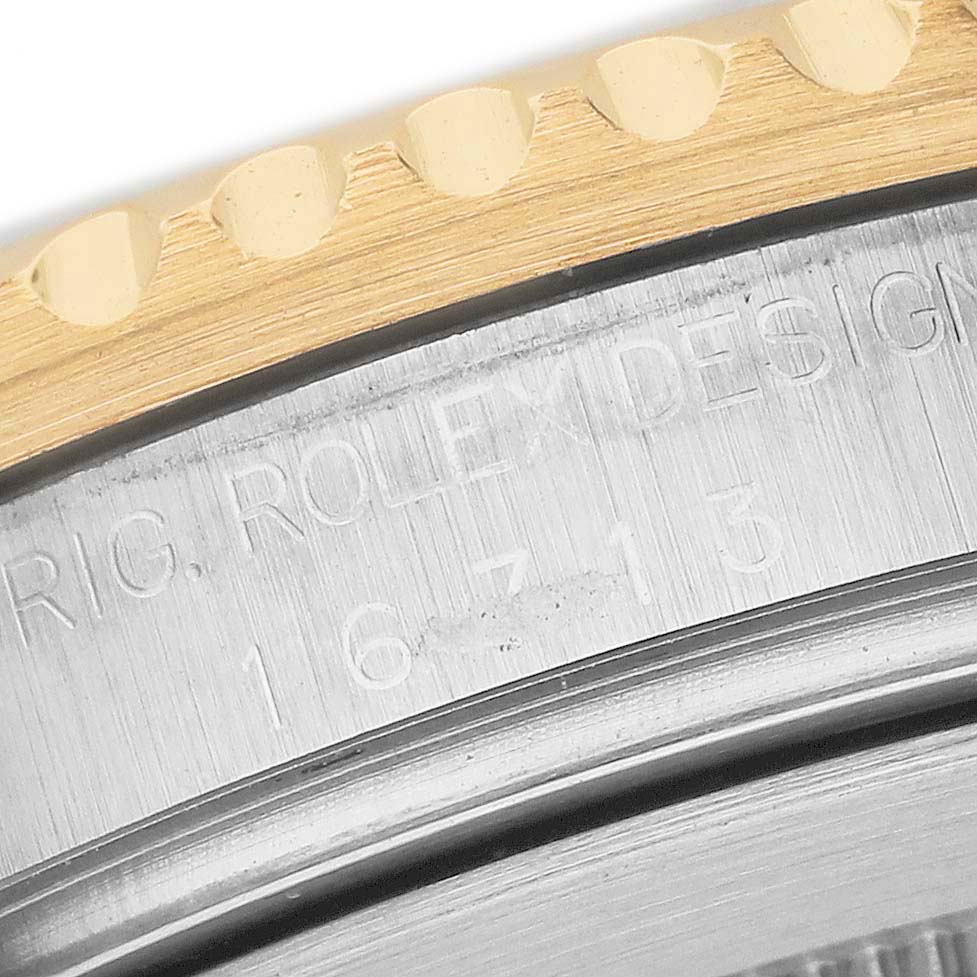 The image shows a close-up of the Rolex GMT-Master 16713LN Men's Stainless Steel Black Dial's gold bezel edge and engraved model number on the case.