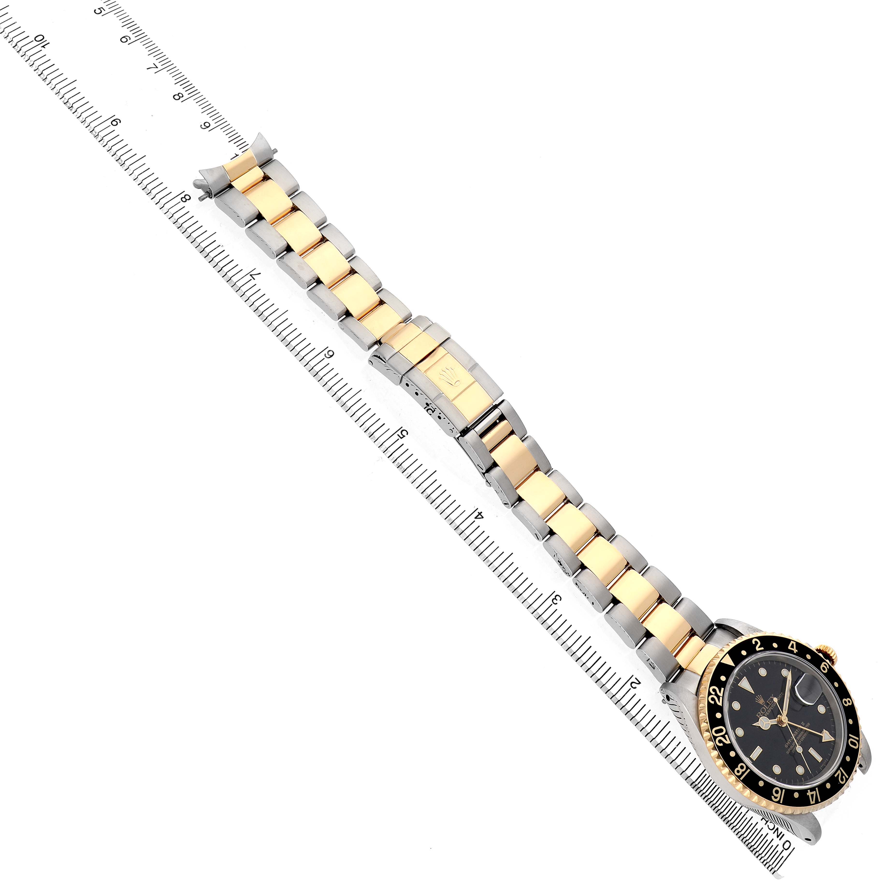 The Rolex GMT-Master 16713LN Men's Stainless Steel Black Dial watch is shown at a top-down angle, highlighting the full bracelet, clasp, and watch face placed alongside a ruler.