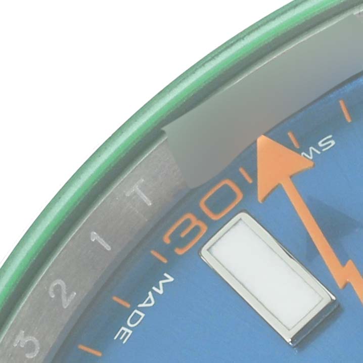 Close-up of a Milgauss Rolex watch showing the orange second hand, minute markers, and part of the blue dial.