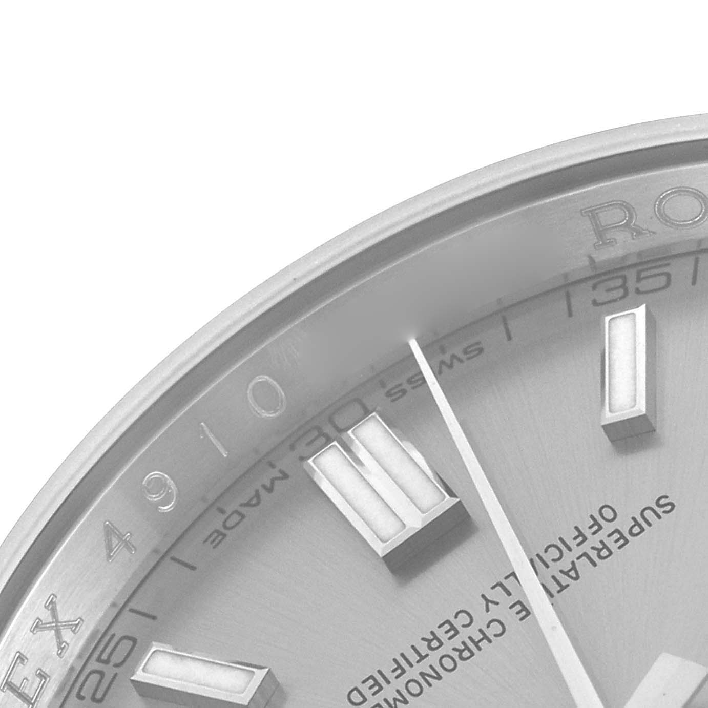 The image shows a close-up of the Rolex Oyster Perpetual 116000 Men
s Stainless Steel Silver Dial 116000 Men
s Stainless Steel Silver Dial watch face, detailing the hour markers and partial brand logo.