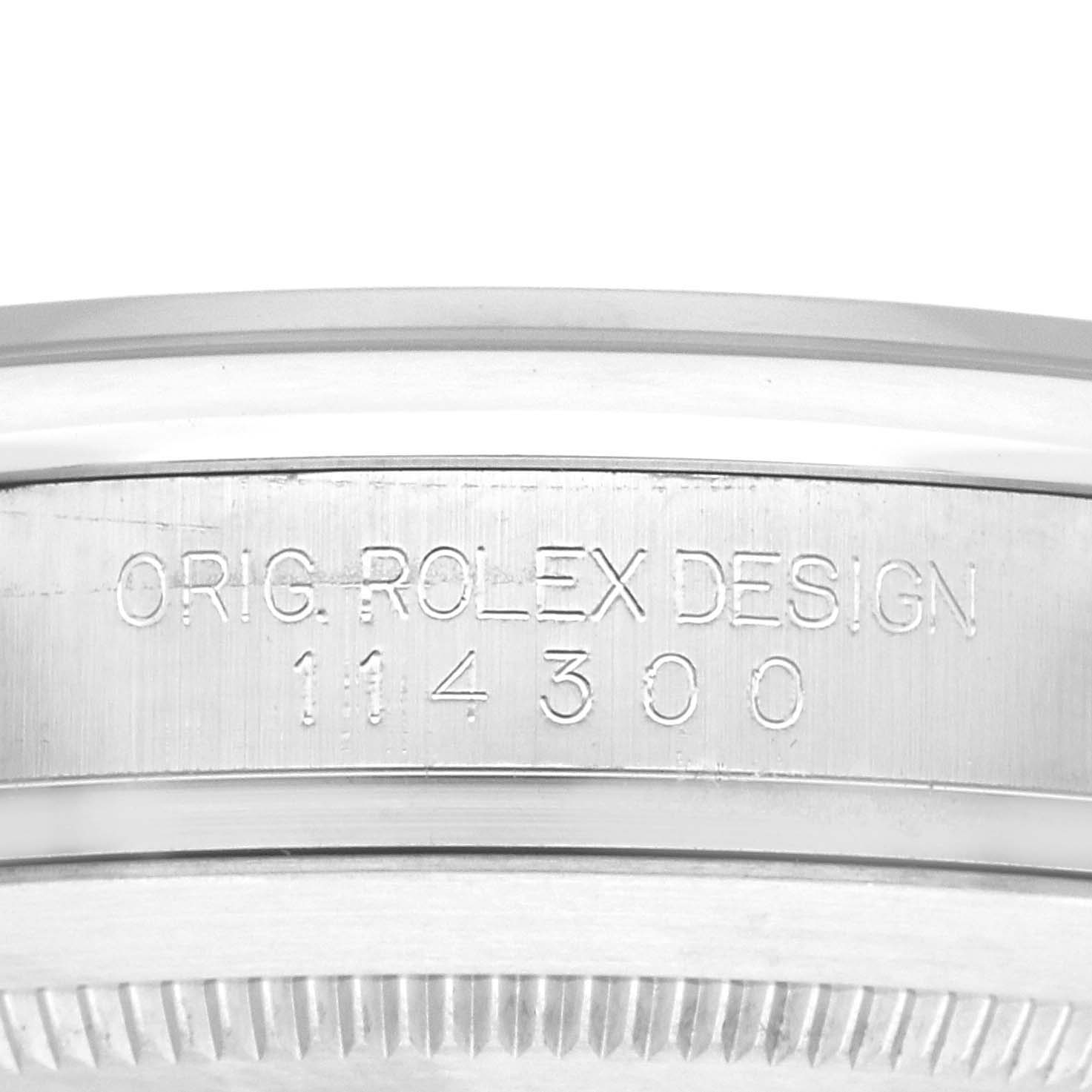 The image shows the side view of a Rolex Oyster Perpetual 114300 Men
s Stainless Steel Blue Dial 114300 Men
s Stainless Steel Blue Dial watch, focusing on its engraved case design number.