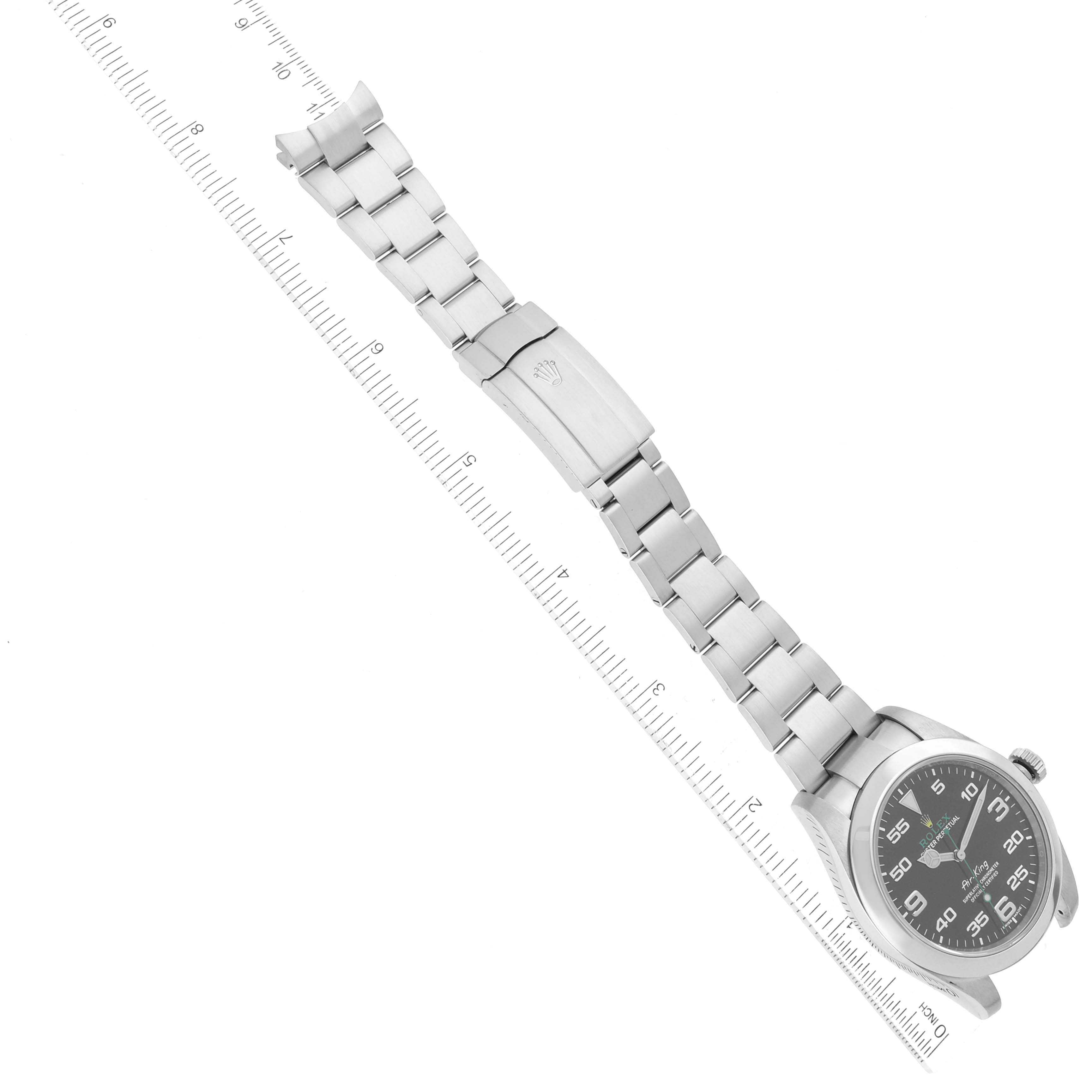 The image shows an overhead view of a Rolex Air-King 116900 Men's Stainless Steel Black Dial 116900 Men's Stainless Steel Black Dial watch, focusing on the face, bracelet, and clasp next to a ruler.
