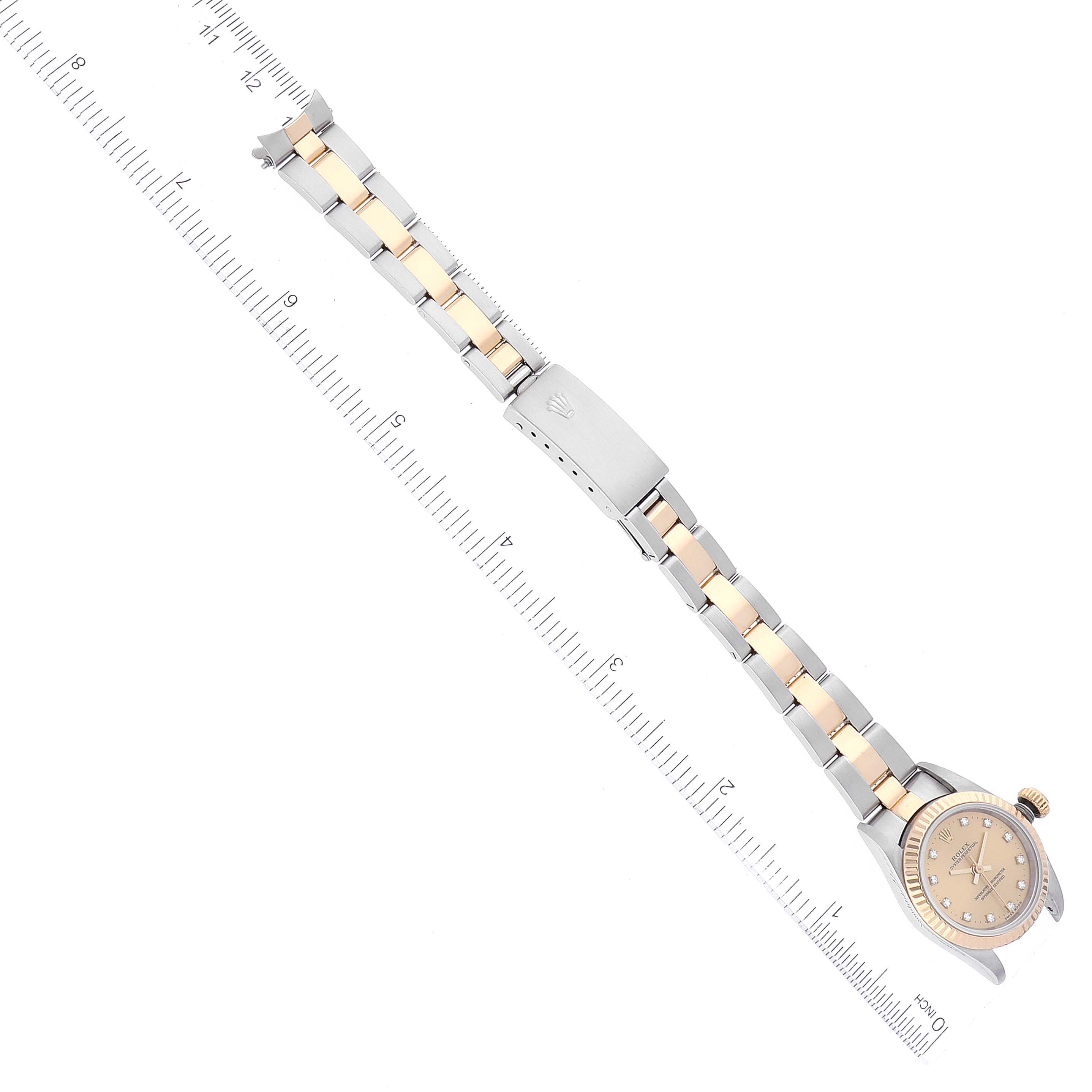 The image shows an overhead view of a Rolex Oyster Perpetual 76193 Women's Steel and Gold (two tone) Champagne Dial 76193 Women's Steel and Gold (two tone) Champagne Dial watch, featuring its full bracelet and clasp with a ruler for scale.