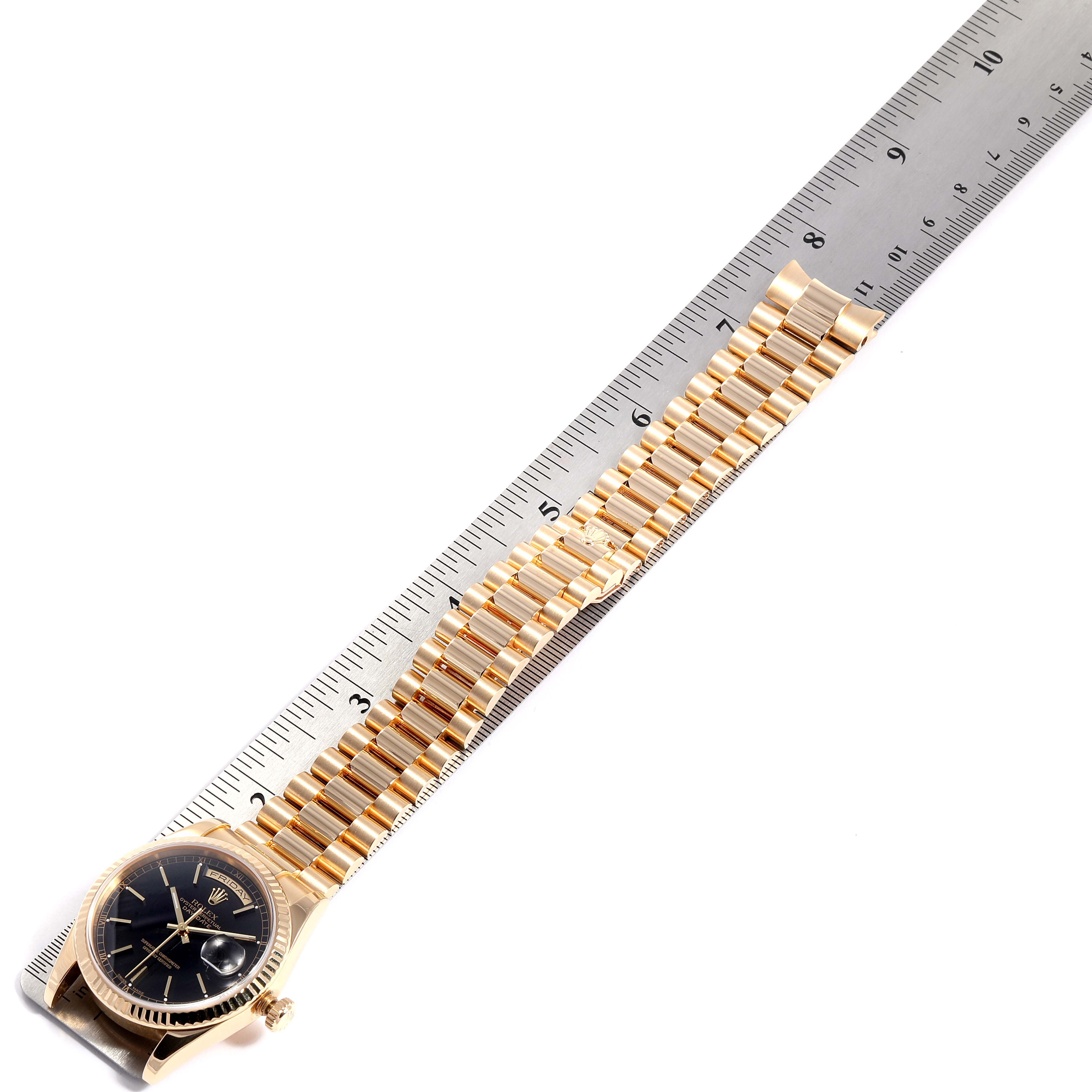 This image shows a Rolex President 118238 Men
s Yellow Gold Black Dial 118238 Men
s Yellow Gold Black Dial model watch positioned diagonally next to a measuring ruler, highlighting the watch face and bracelet.