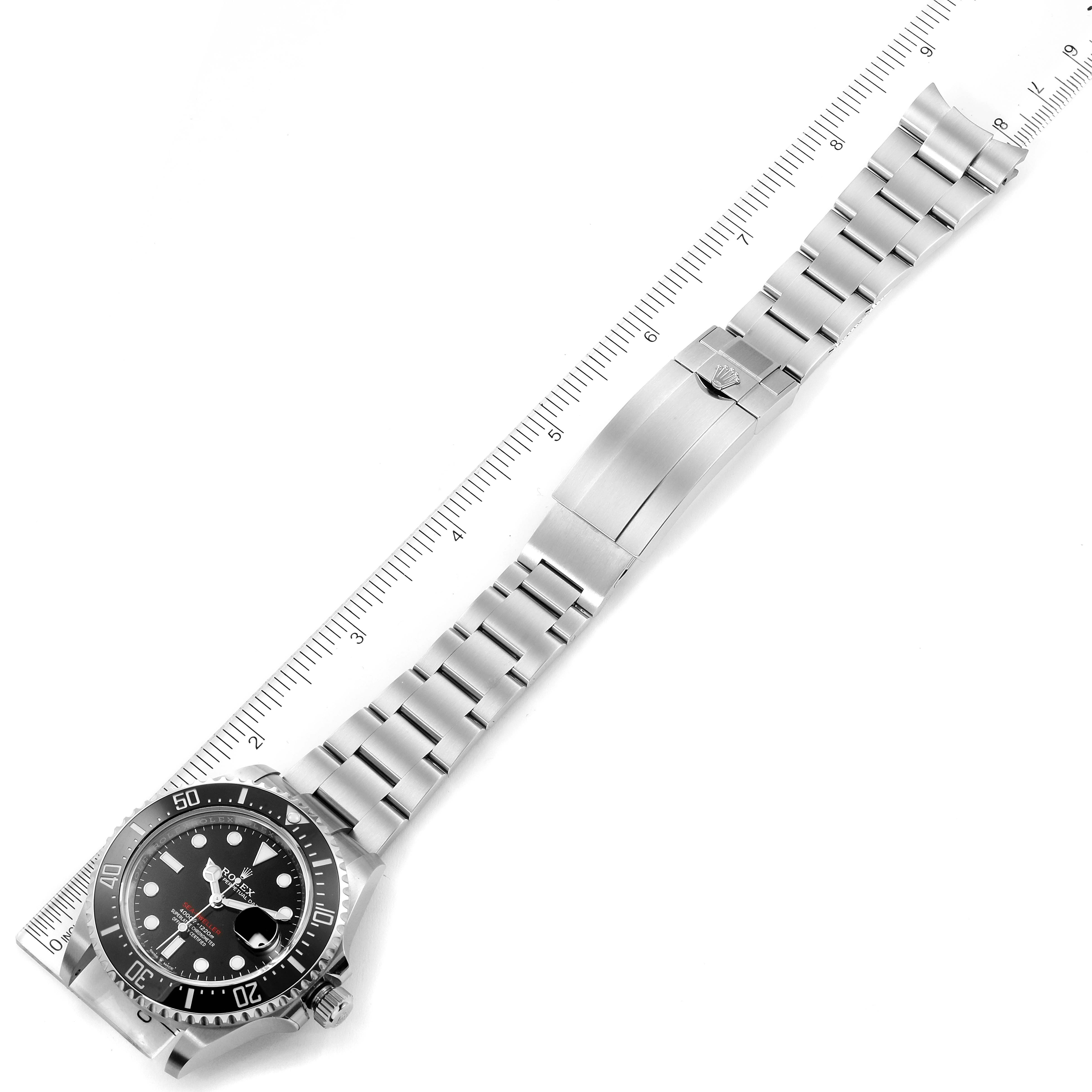 The image showcases a full frontal view of a Rolex Sea-Dweller 126600 Men
s Stainless Steel Black Dial 126600 Men
s Stainless Steel Black Dial watch, emphasizing its face, bezel, and bracelet alongside a ruler for scale.