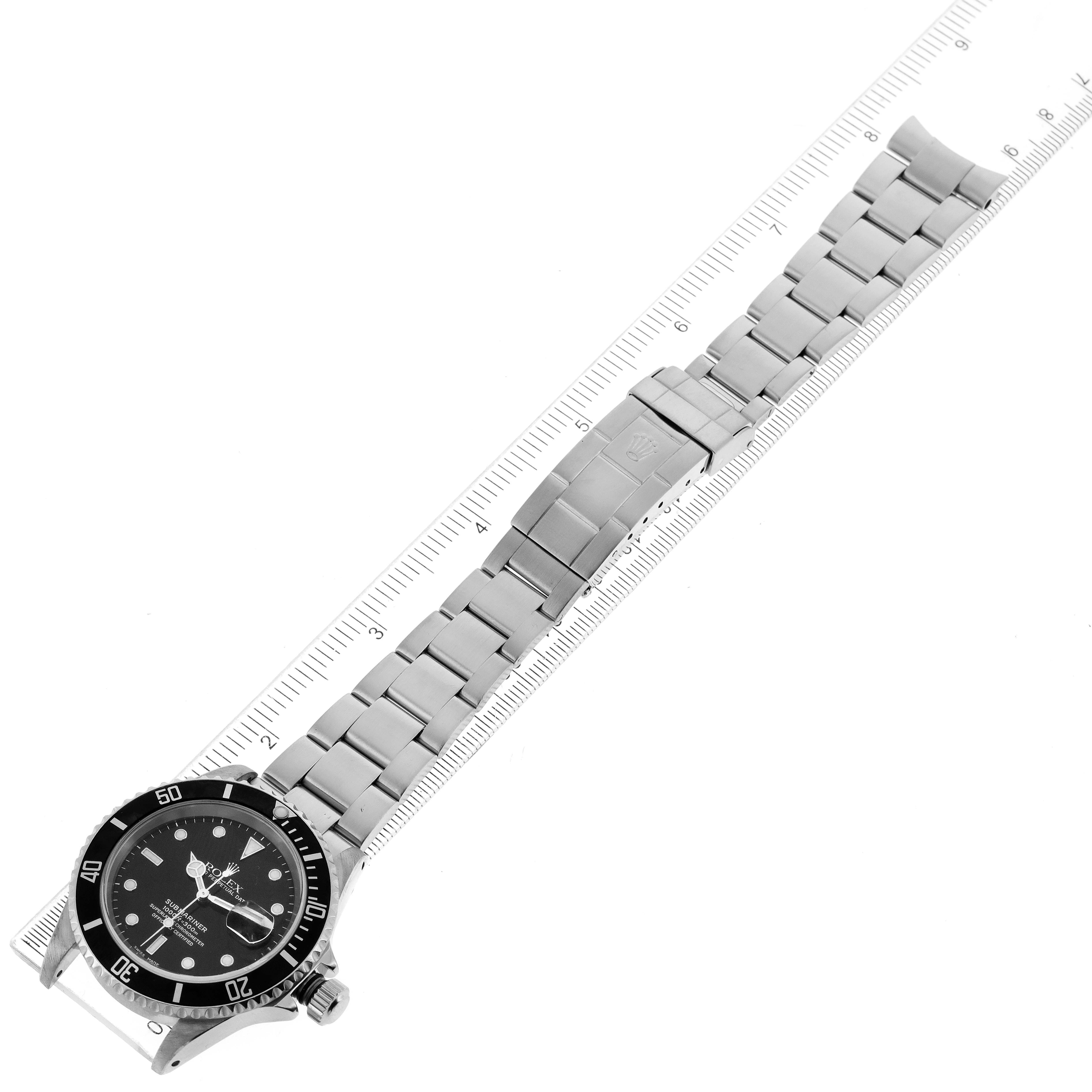 The Rolex Submariner 16610 Men
s Stainless Steel Black Dial 16610 Men
s Stainless Steel Black Dial watch is shown laid flat alongside a ruler, highlighting the bracelet and dial.